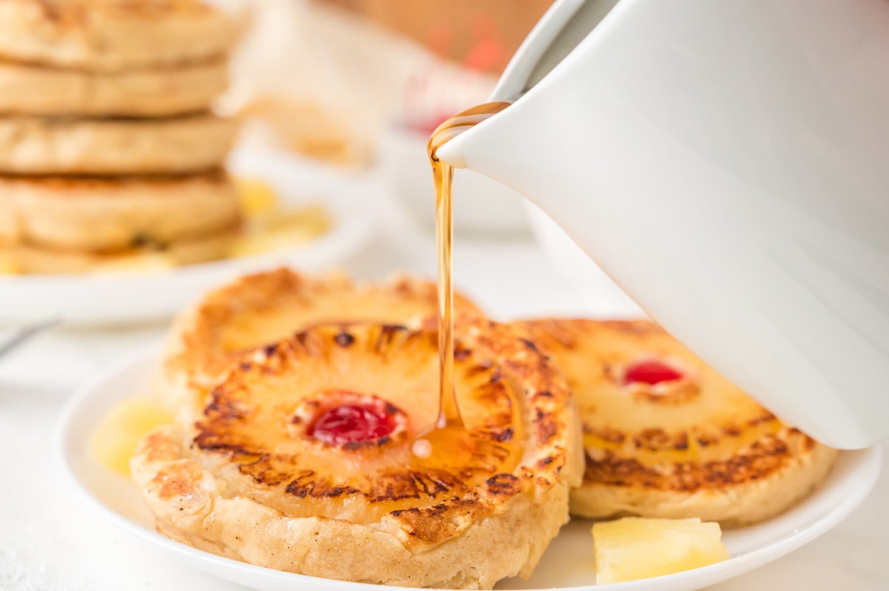 pouring syrup on top of pineapple upside down pancakes