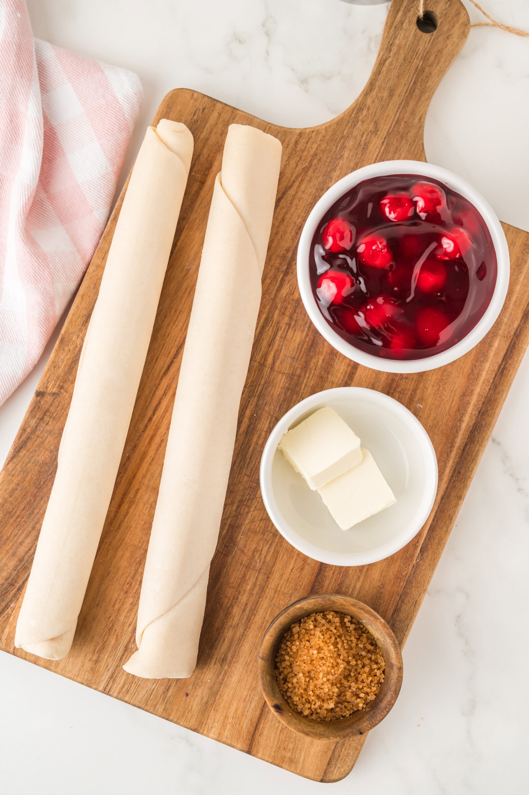 All ingredients placed out ready to make Cherry Pie Cookies, pie dough, cherry pie filling, sugar and butter