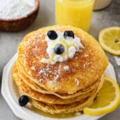 A small stack of lemon ricotta pancakes ready to be served and enjoyed. There's fresh blueberries, whip cream and a lemon glaze
