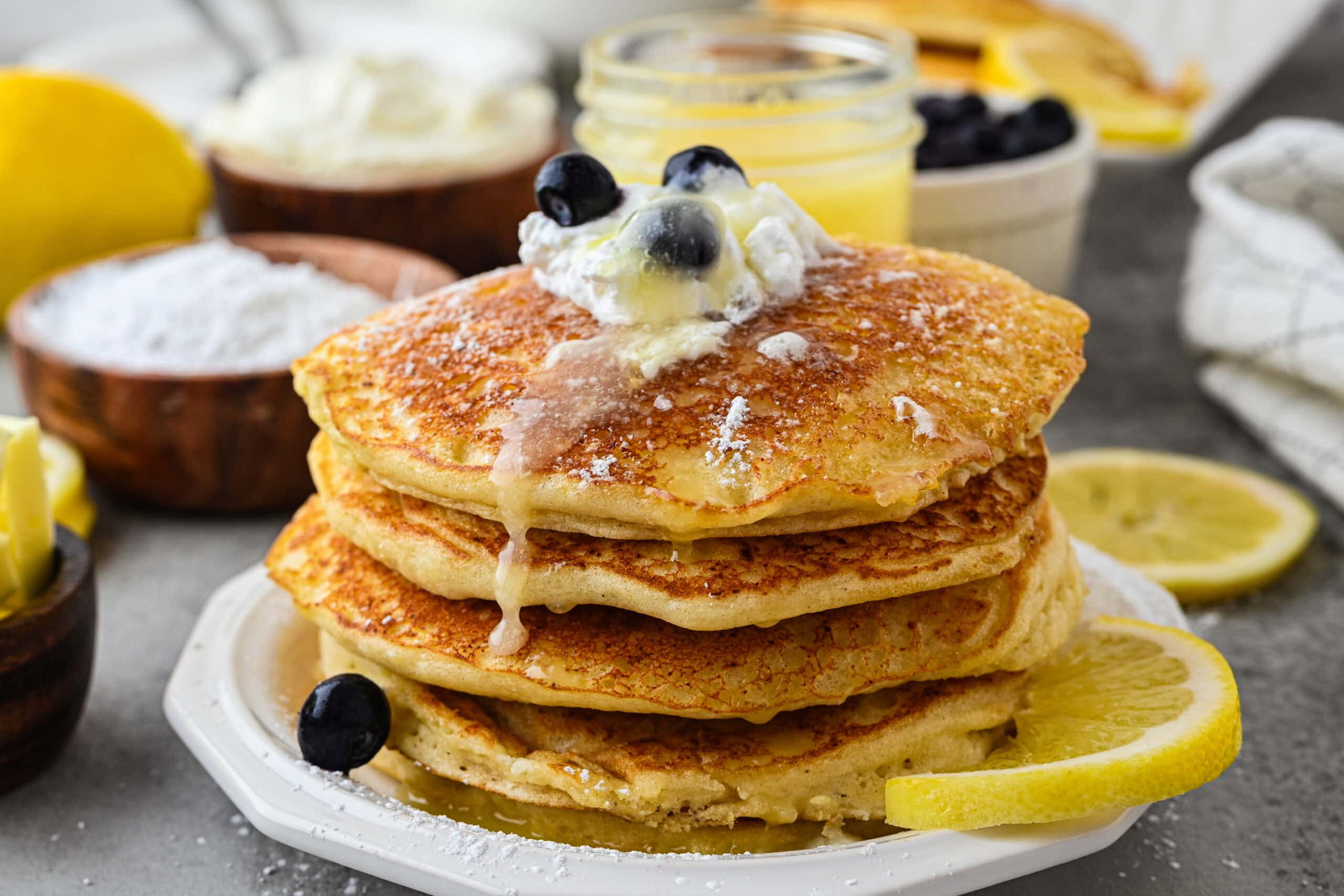 Lemon Ricotta Pancakes stacked tall with fresh blueberries, lemon glaze and whip cream