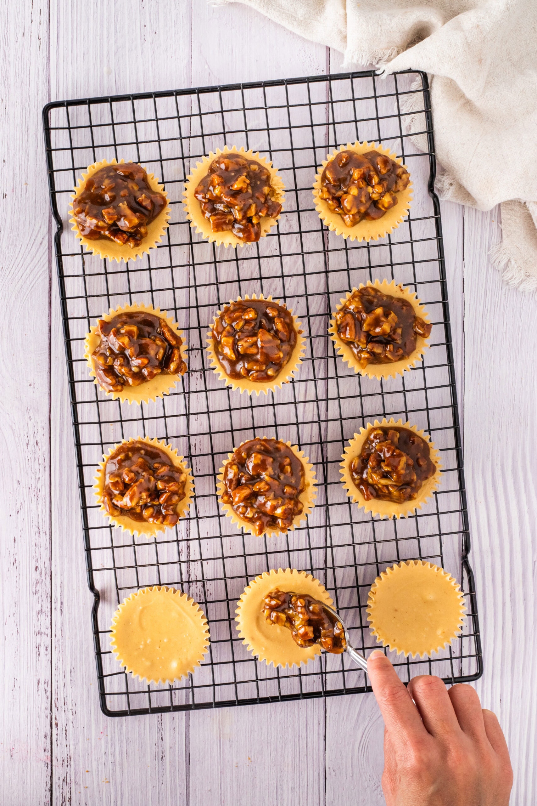 Pecan filling being placed on top of baked cheesecake layer in muffin tin