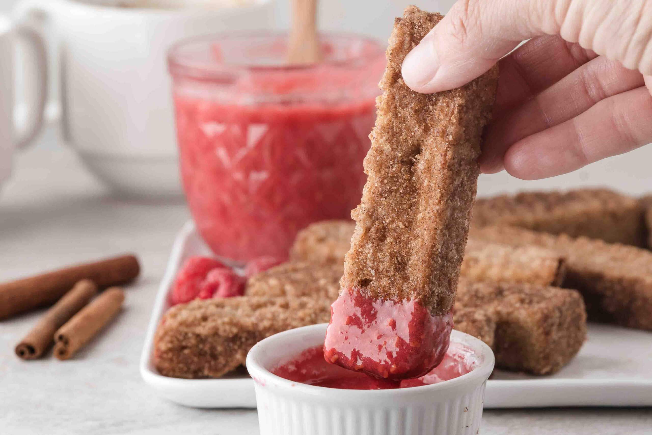 French toast stick being dipped in raspberry sauce ready to be eaten