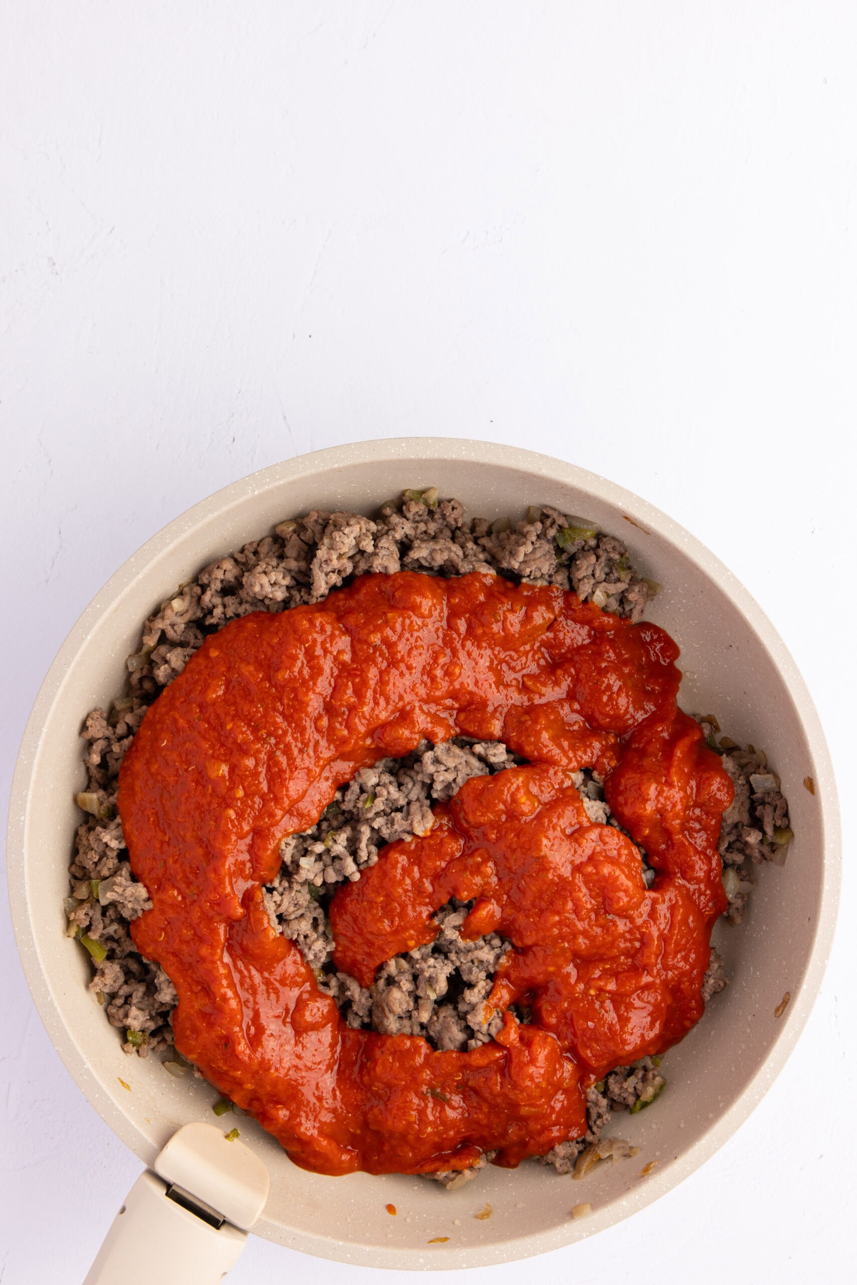 Process of adding canned tomatoes to the ground beff and spices