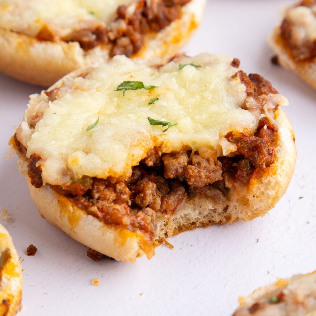 Close up of pizza burger with a bite taken out of it to see the layers of bun, ground beef and mozzarella cheese