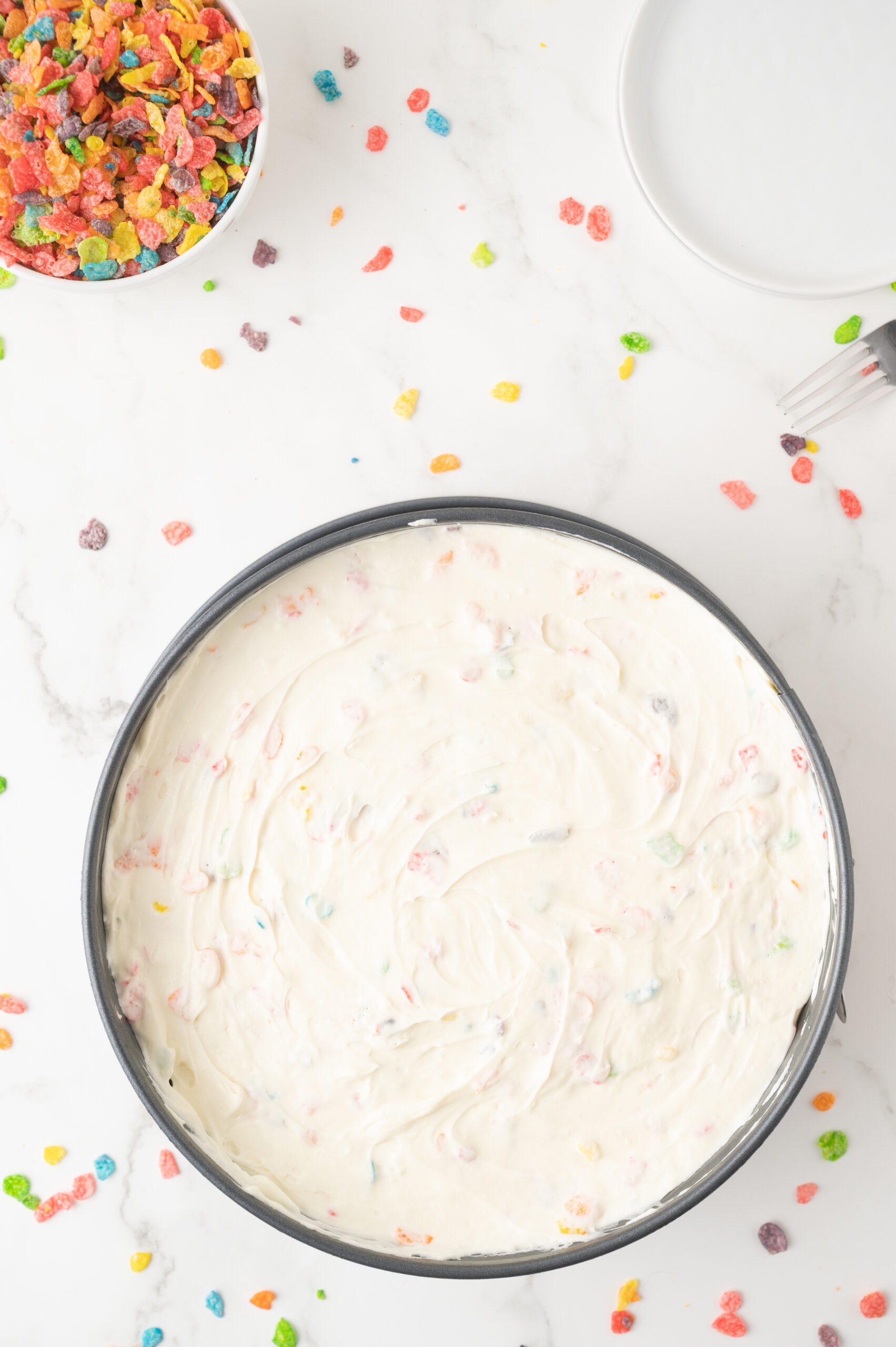 The last step of the process of making fruity pebble cheesecake, folding in the cool whip with fruity pebbles