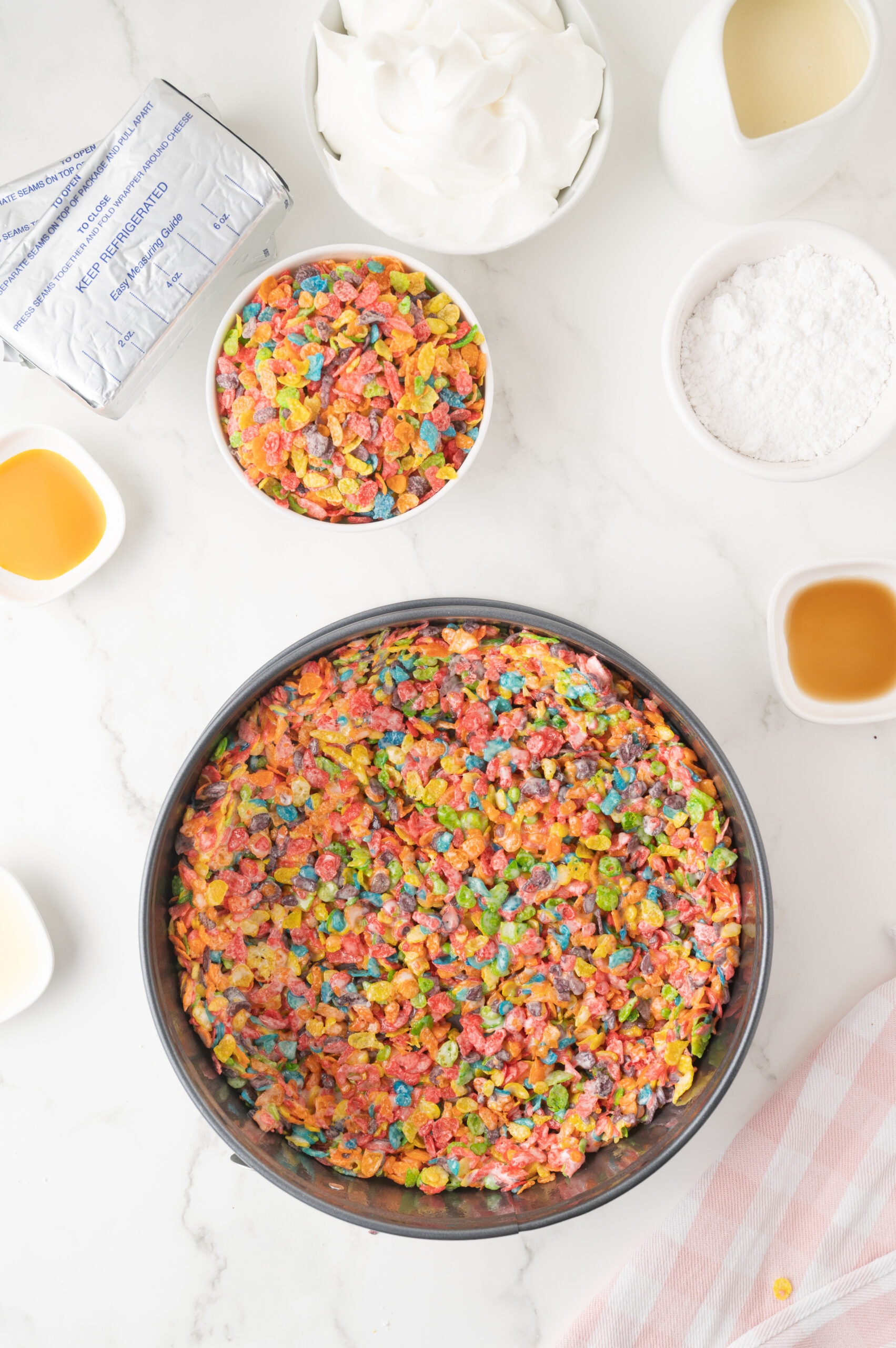 The fruity pebbles being added on top to the cheesecake batter