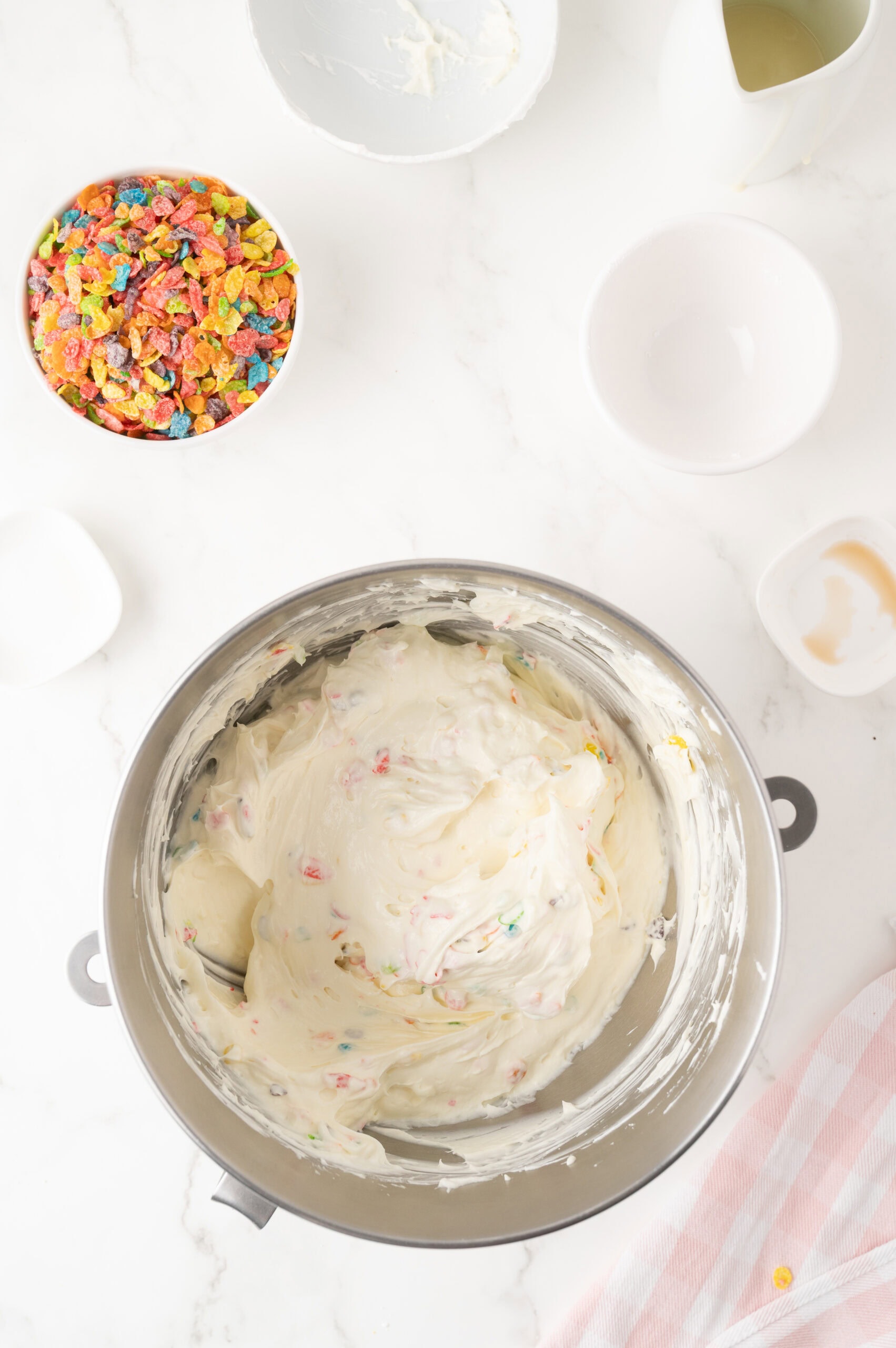 Mixing the batter of cream cheese and fruity pebbles, sweet condensed milk and then continuing the process to add more ingredients