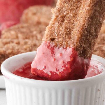 Air Fryer french toast stick being dipped in homemade raspberry sauce