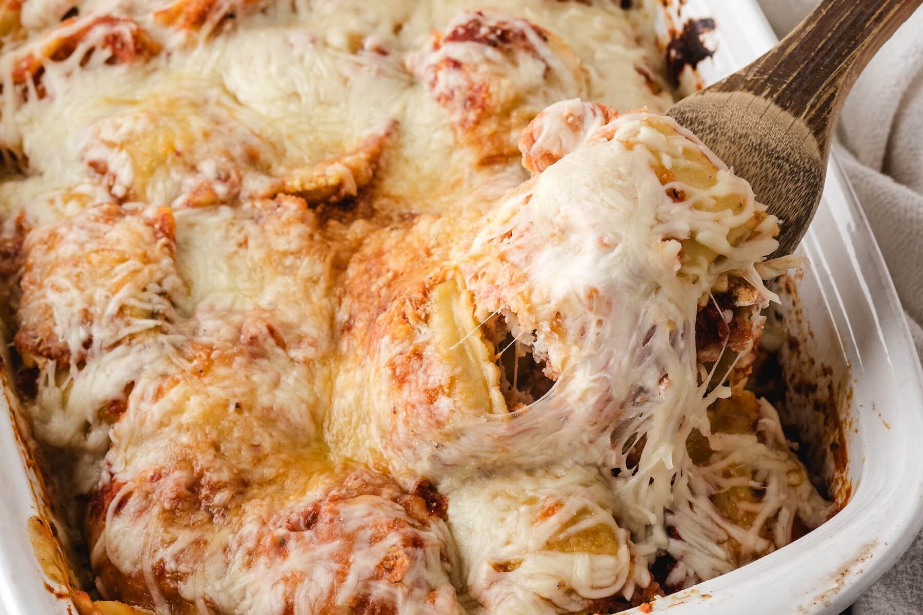 baked ravioli casserole covered in melted cheese and marinara sauce with a wooden spoon