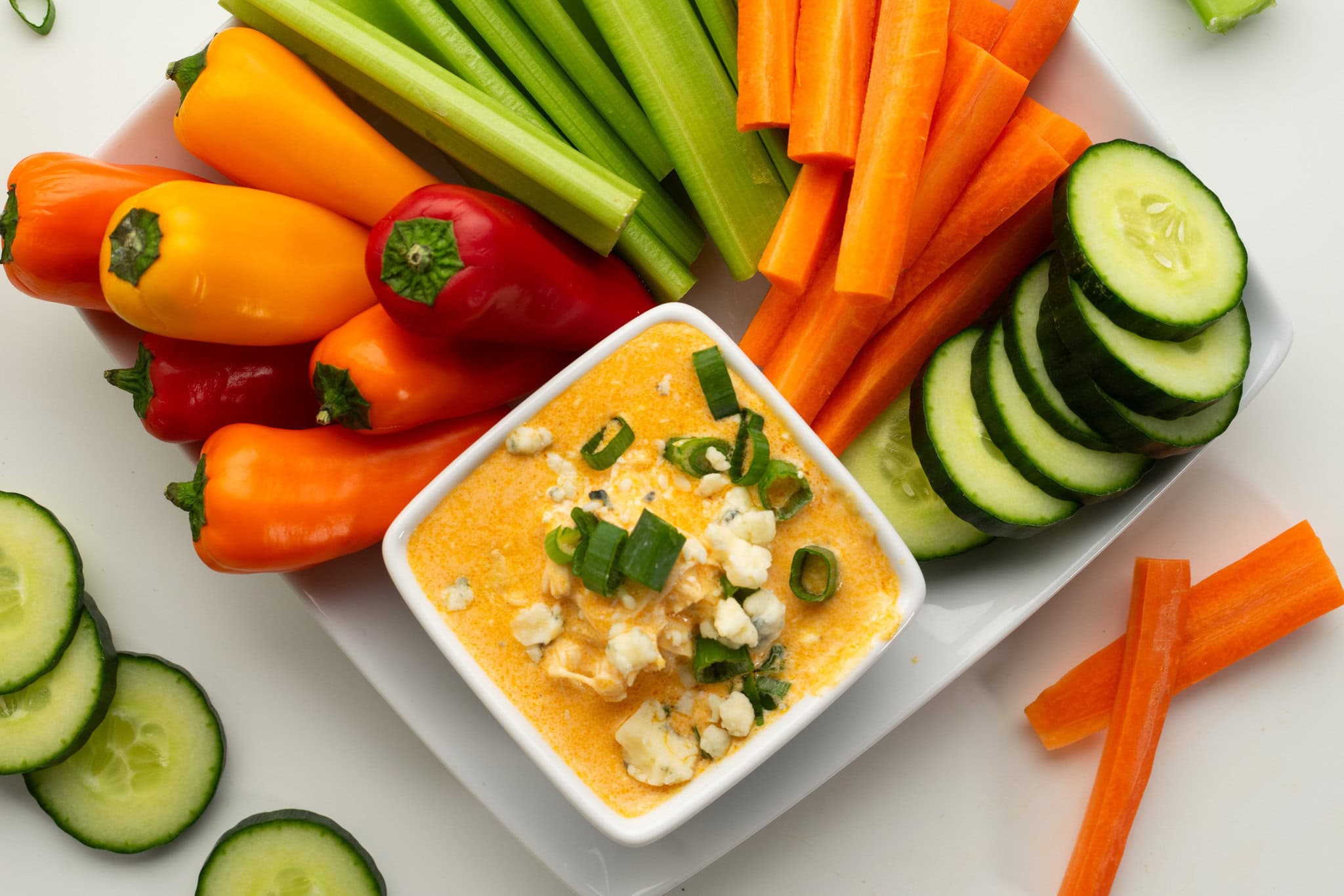 Buffalo Chicken dip is served in a square dish, garnished and ready to be enjoyed with carrots, cucumbers, peppers, celery