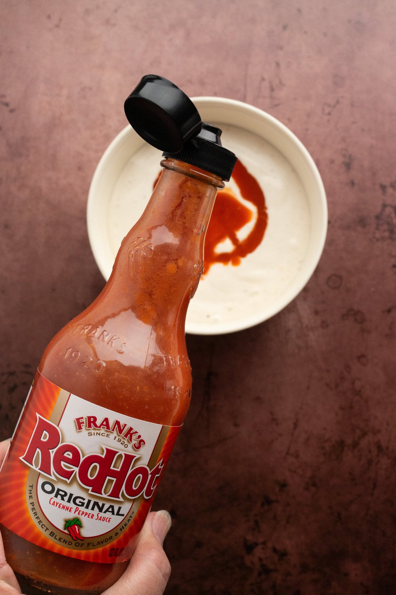 Starting the process of making buffalo chicken dip. Adding Franks' Red Hot sauce to a bowl