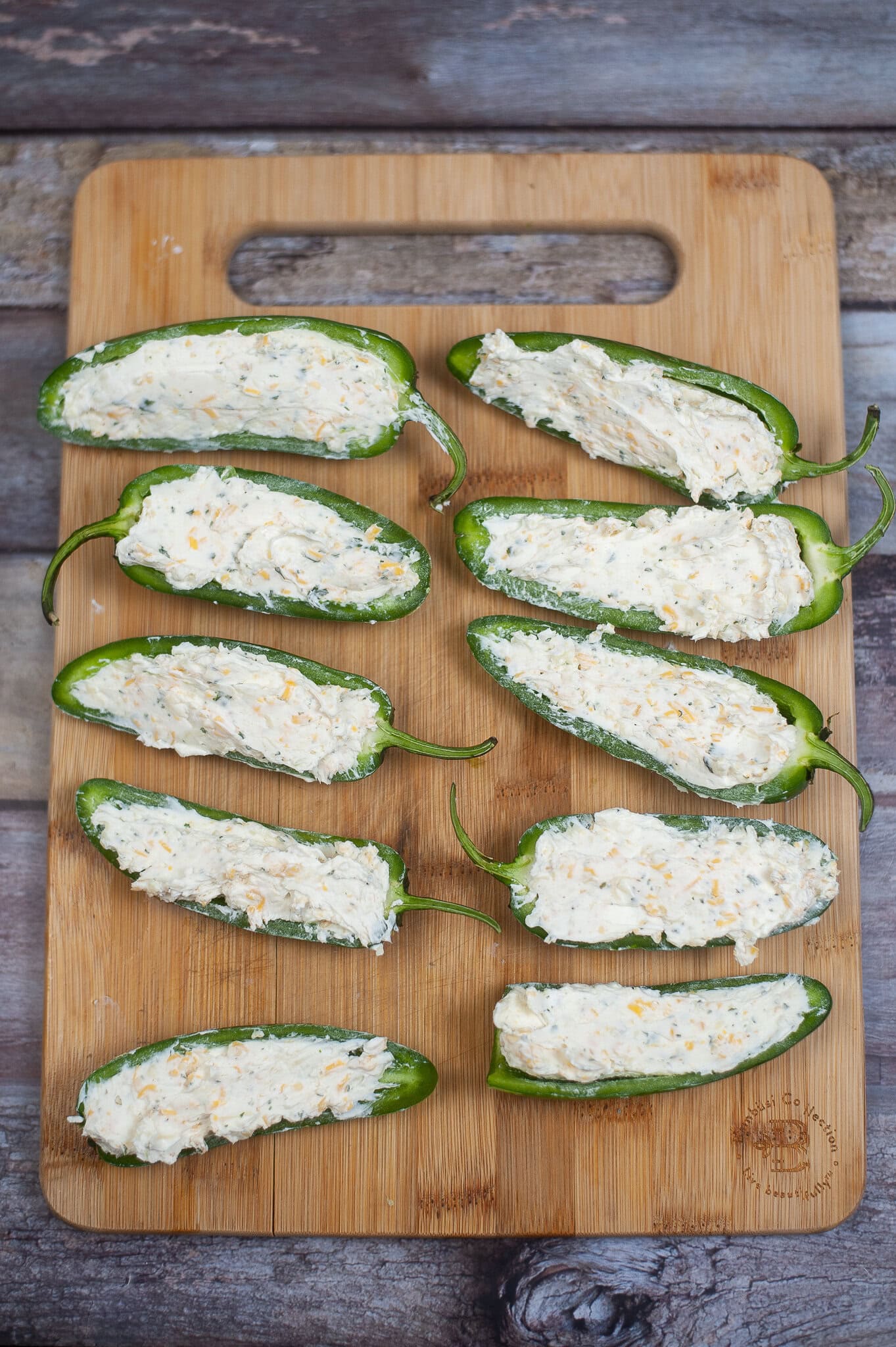 The process of adding cheeses and adding it to scooped out jalapenos.