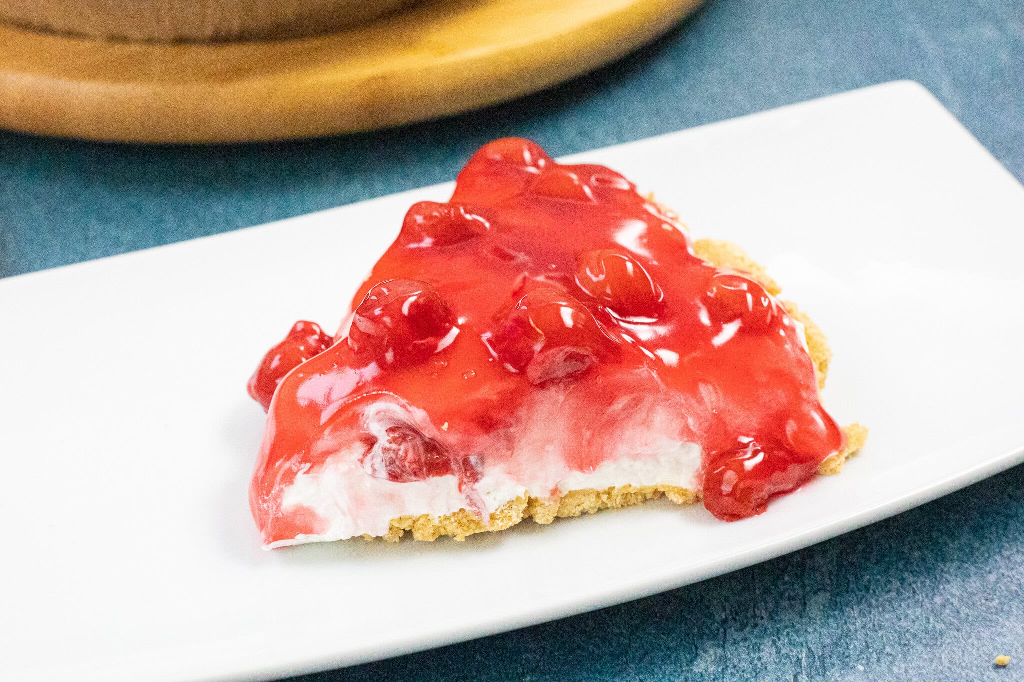 A slice of no bake cherry cheesecake on a plate, positioned to the side to see all the layers, ready to be enjoyed