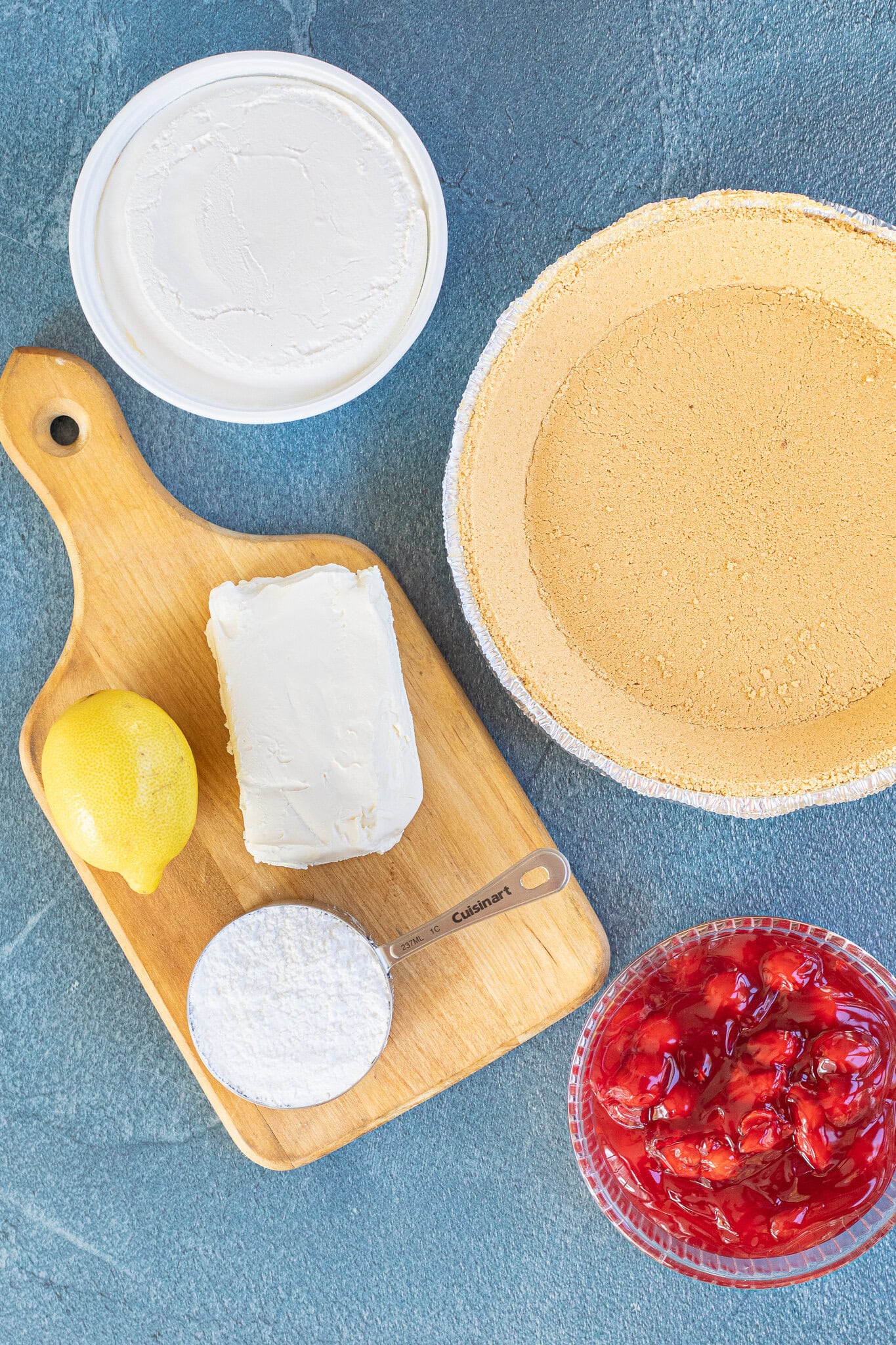 All ingredients pictured: graham cracker crust, cream cheese, cool whip, cherry pie filling, powdered sugar and lemon juice