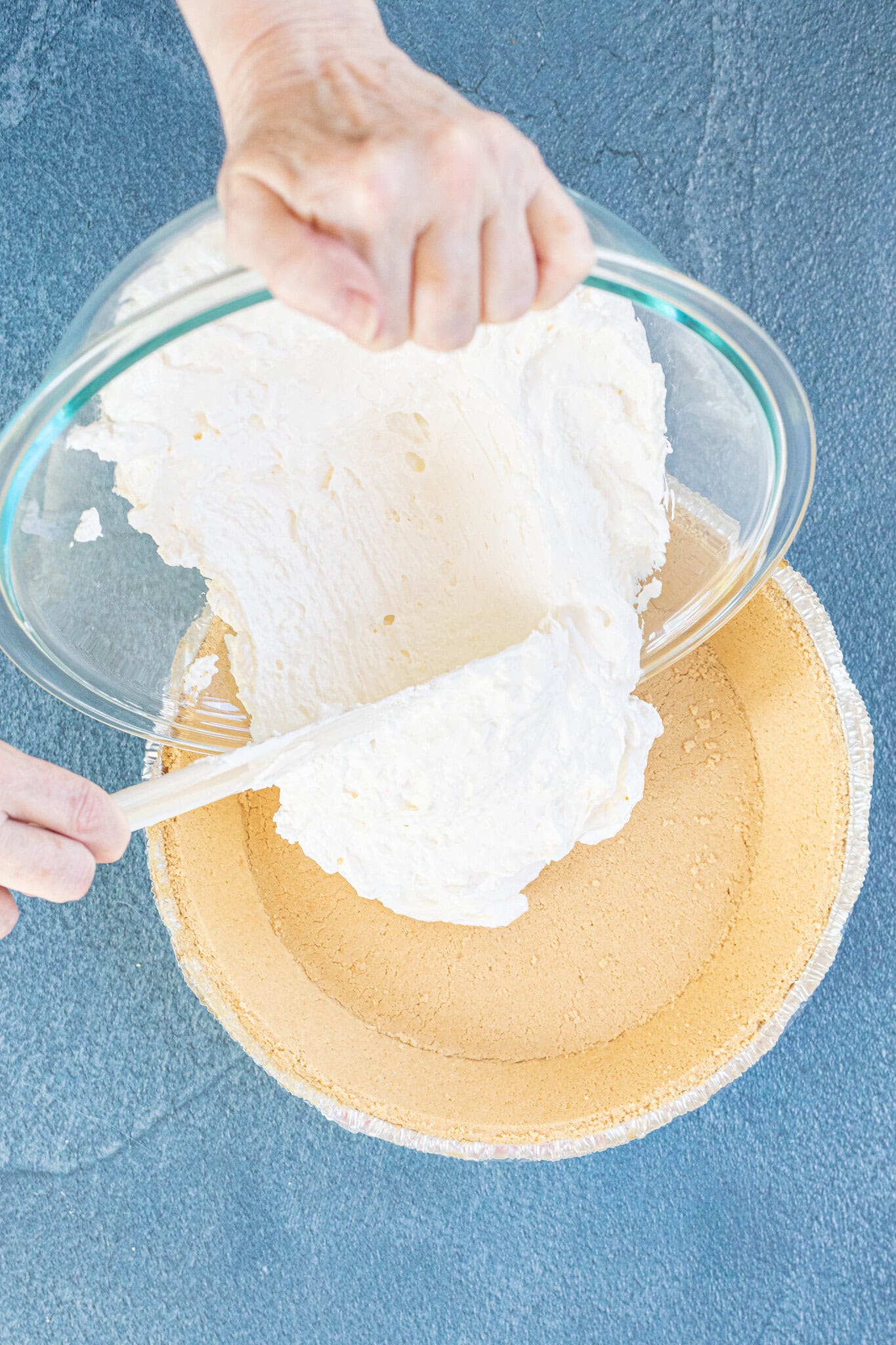 Cream cheese all mixed and creamy being added into the graham cracker crust