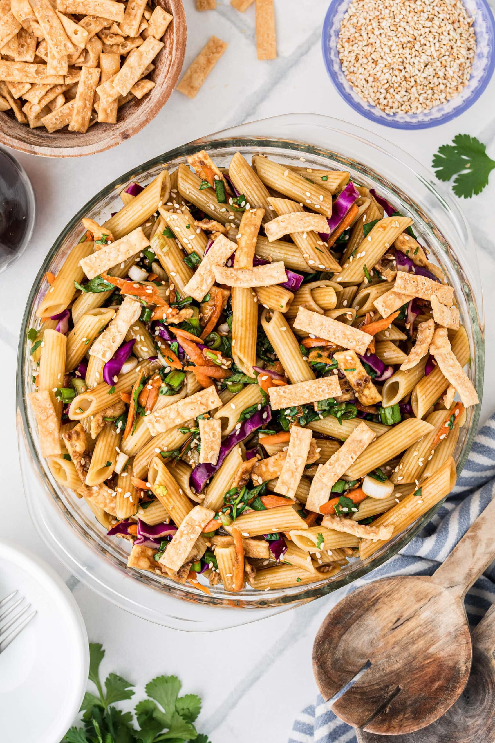 Asian Pasta salad in a glass bowl, plates and serving tools next to it, ready to be served