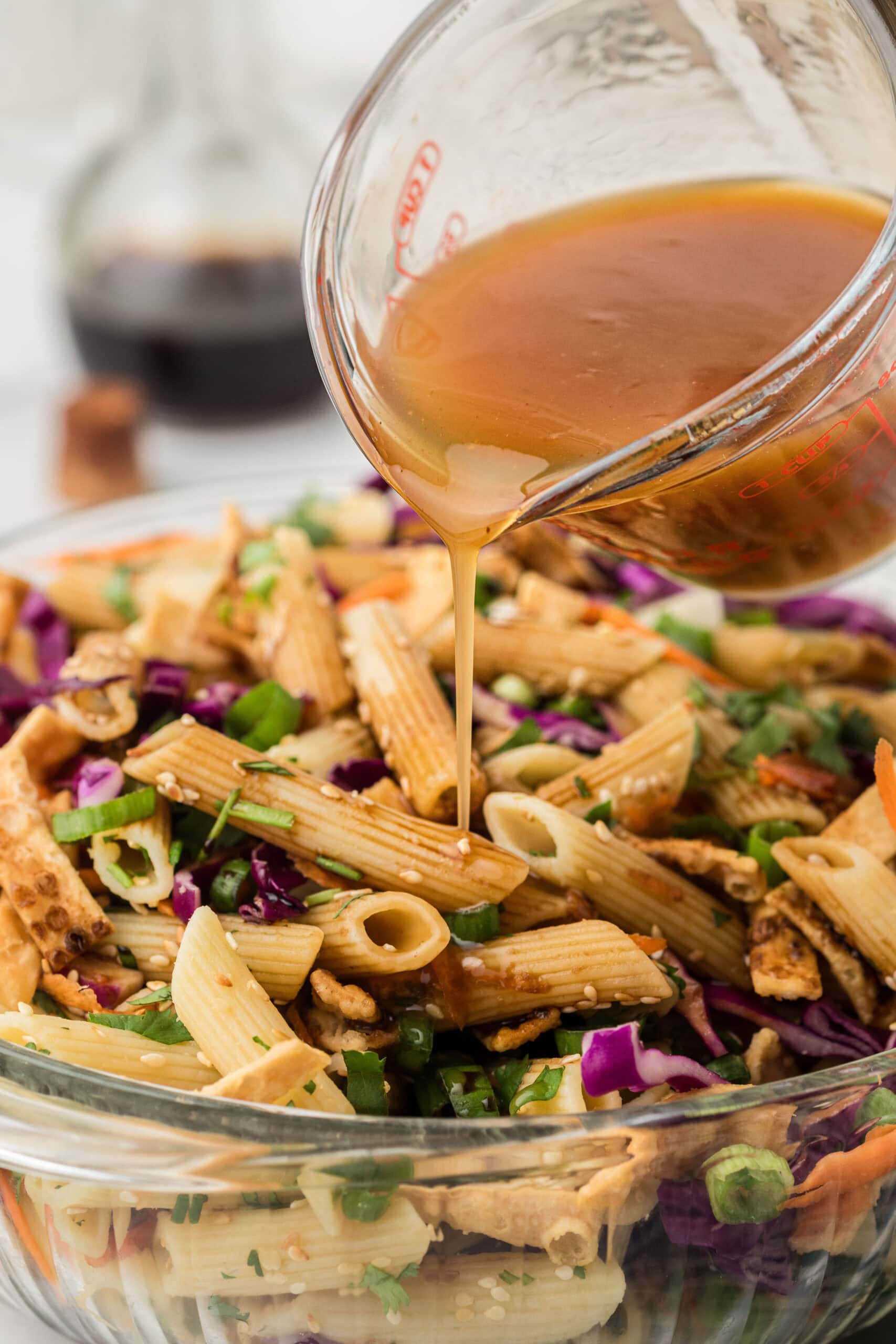 Dressing being poured on the finished Asian pasta salad in a glass bowl