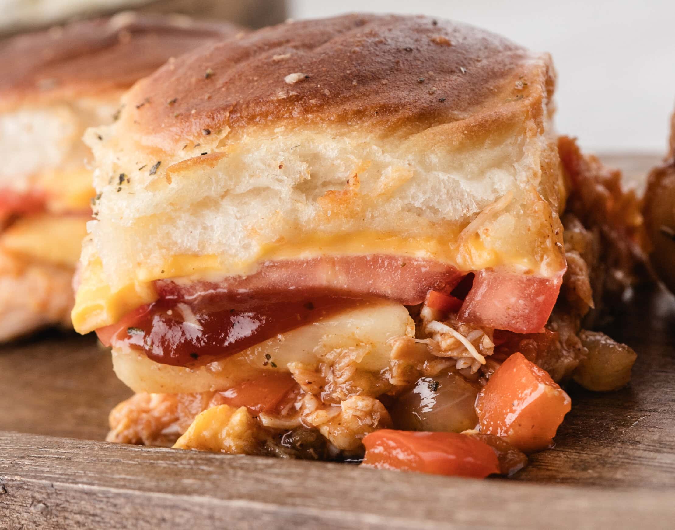 Close up of a BBQ slider, some chicken mixture is falling out out on a wooden board to show the ingredients.