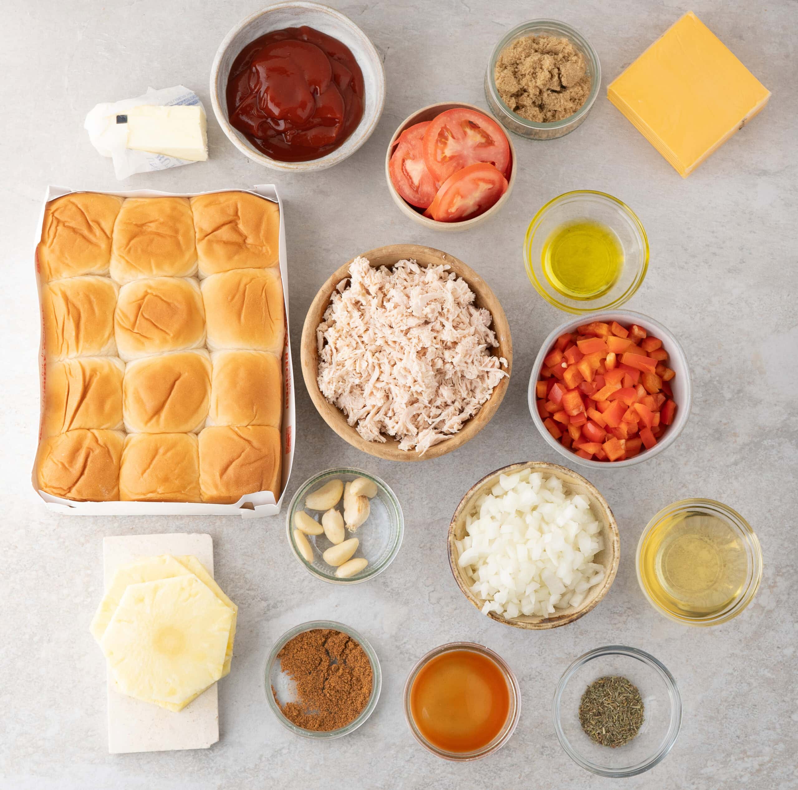 All ingredients pictured:oil, garlic, chicken, BBQ rub, hot sauce, pineapple slices, diced onions, diced tomatoes, tomato, brown sugar, cheddar cheese slices, ketchup, butter, apple cider vinegar, Italian seasoning, and Hawaiian slider rolls.