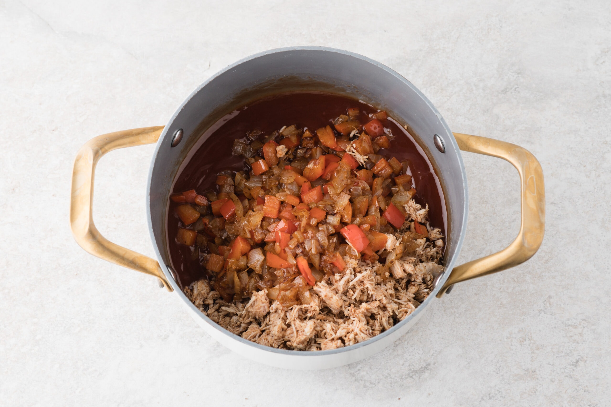 All ingredients in a saucepan, ready to be mixed to add the slider buns: tomatoes, onions, shredded chicken, onion.