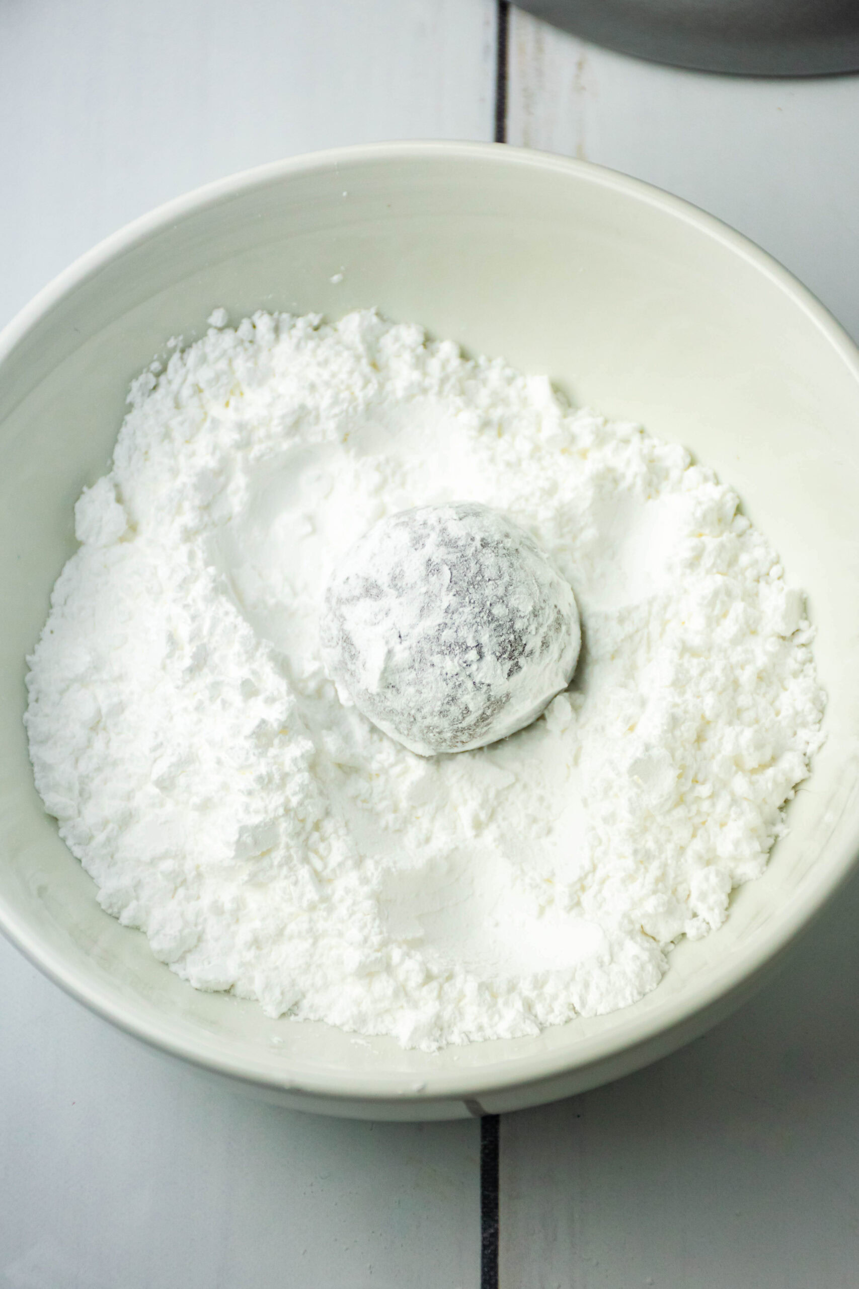 Cookie being rolled in the powdered sugar in a bowl