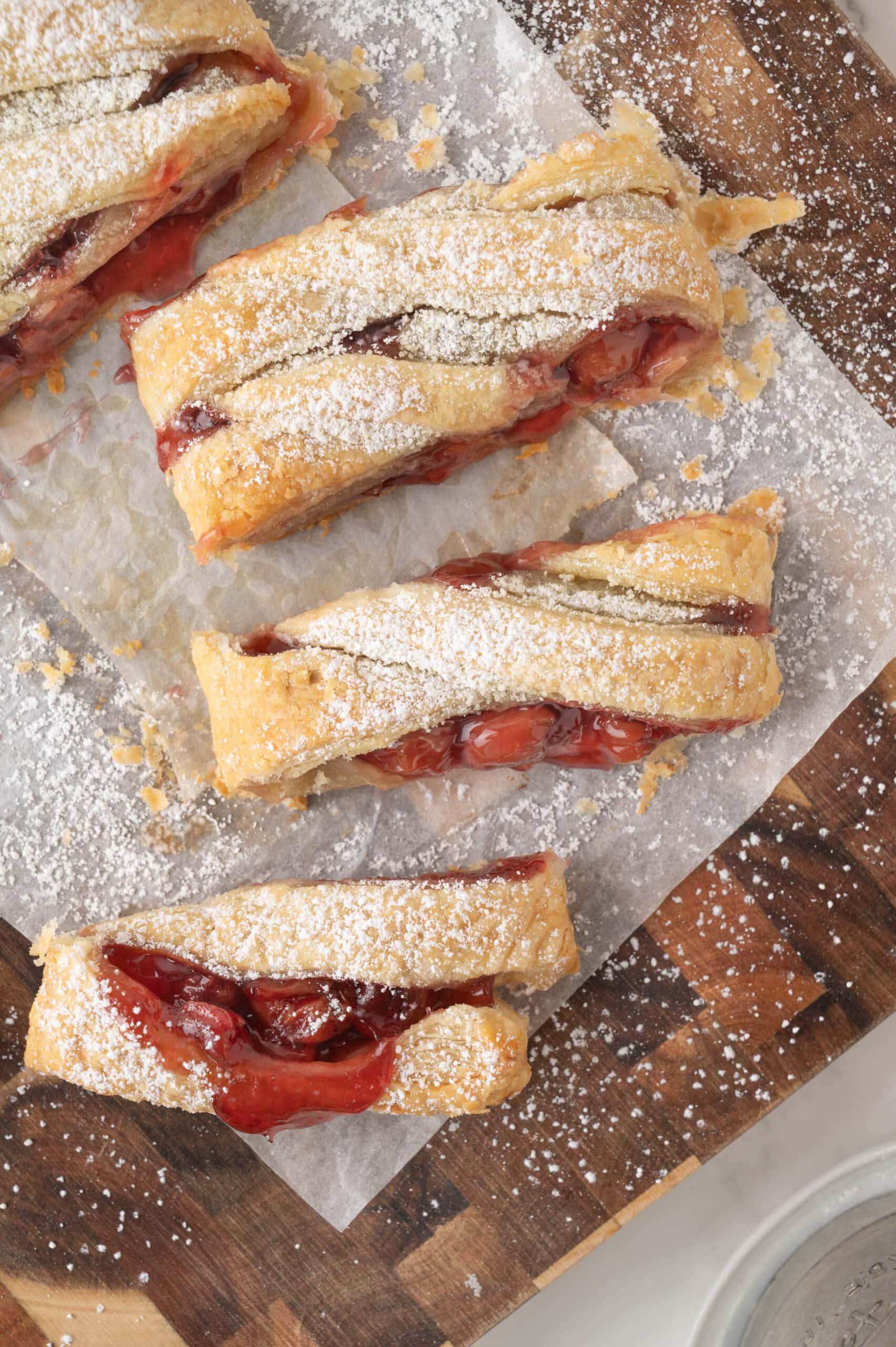Sliced cherry strudel on a wooden board, ready to grab a slice. You can see the texture of the puff pastry and cherry filling