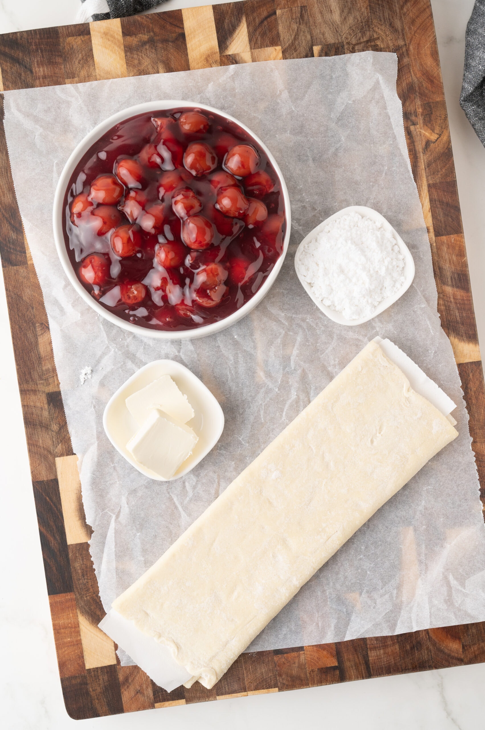 All ingredients to make puff pastry cherry strudel: cherry pie filing, puff pastry, unsalted butter, powdered sugar