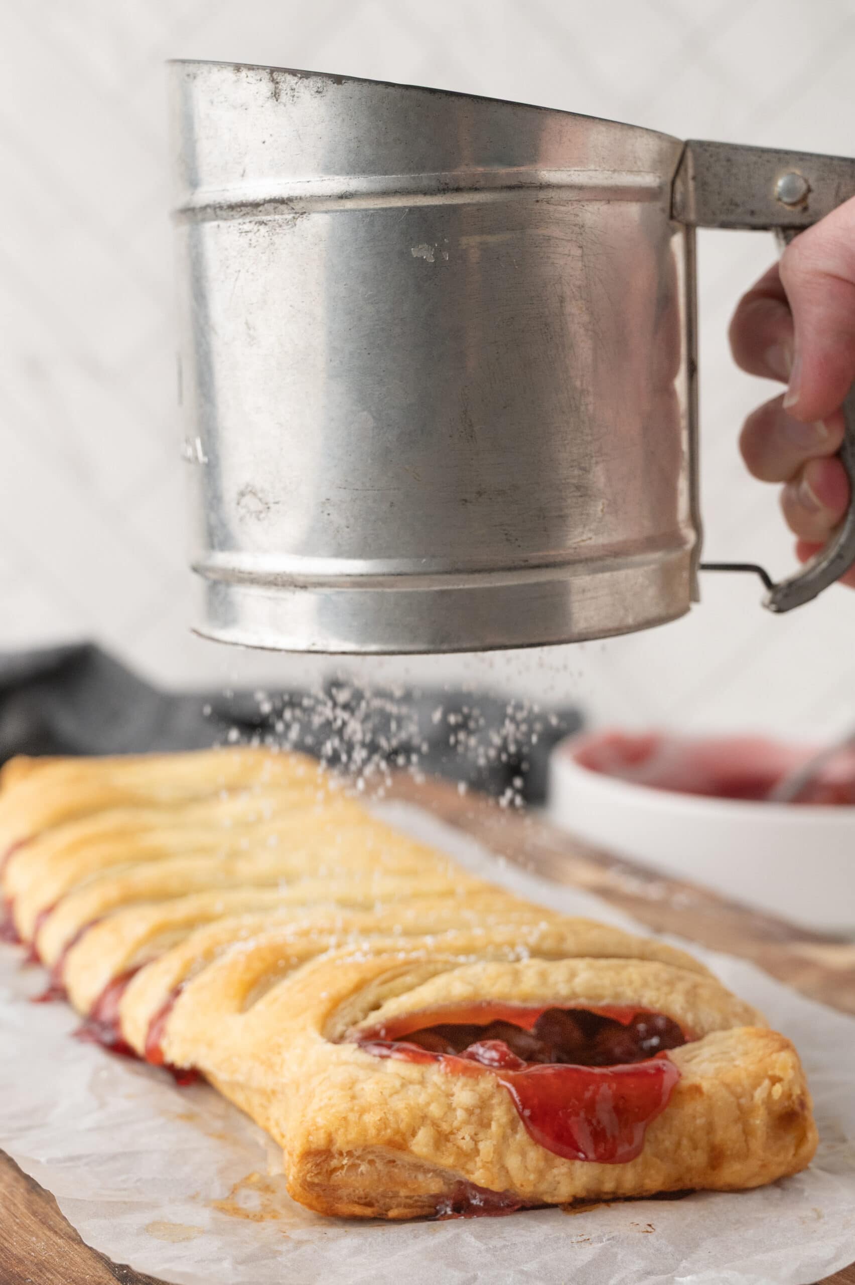 Adding sifted powdered sugar to the top of the puff pastry cherry strudel