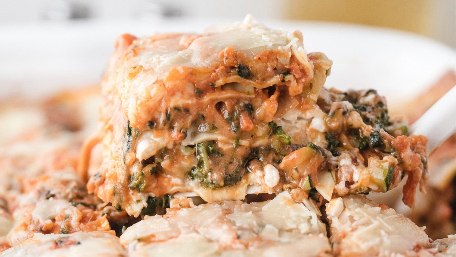 a close up of one piece of veggie lasagna showing zucchini, broccoli, carrots, cheese, and noodles