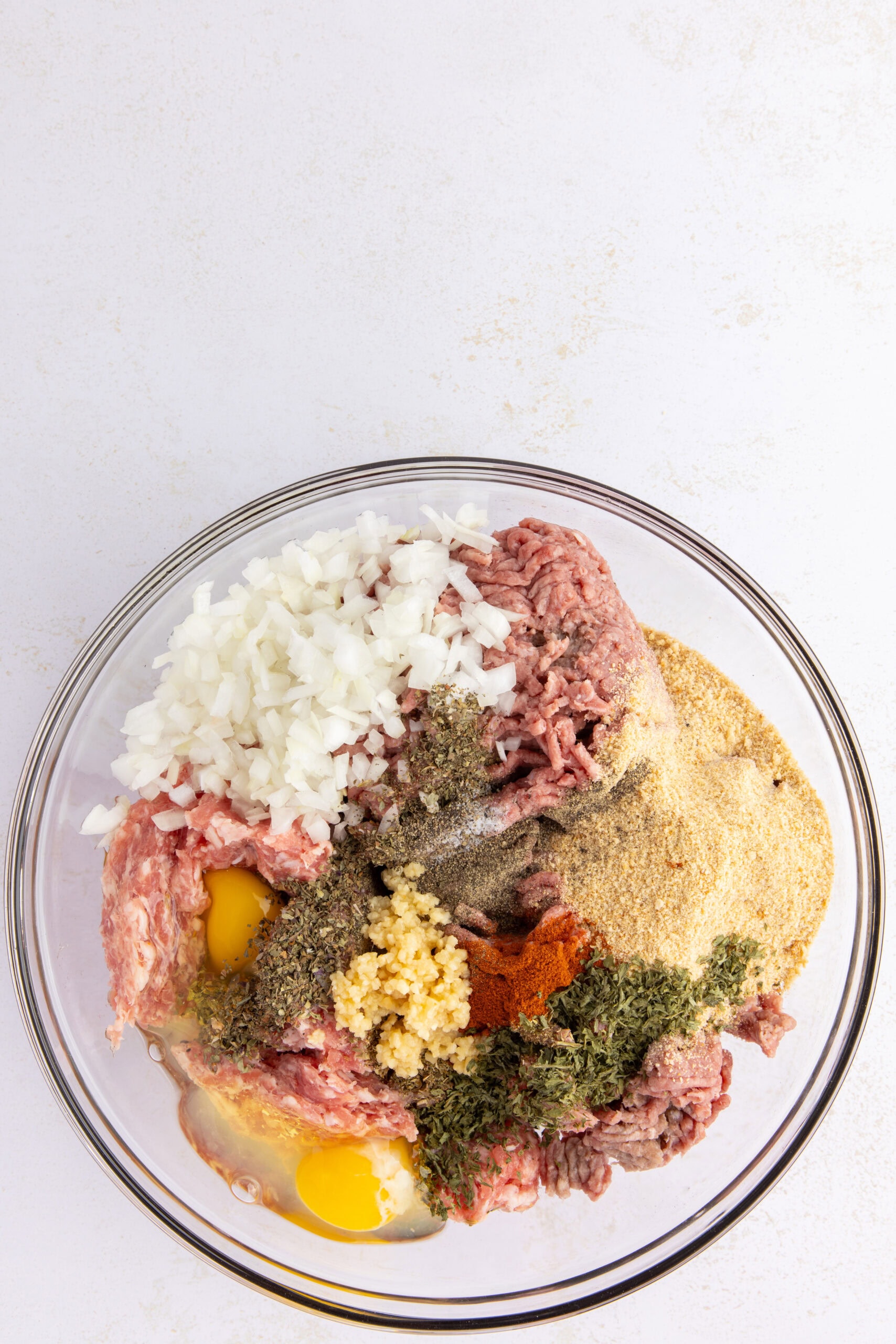 All ingredients in a large glass bowl, ready to be mixed by hands to start the process of making the jumbo mozzarella meatballs.