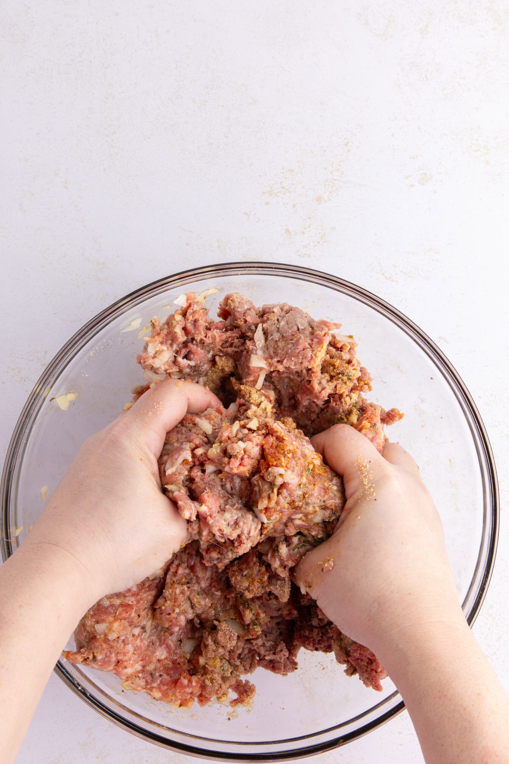 Using your hands, mixing the meatball ingredients in a glass bowl