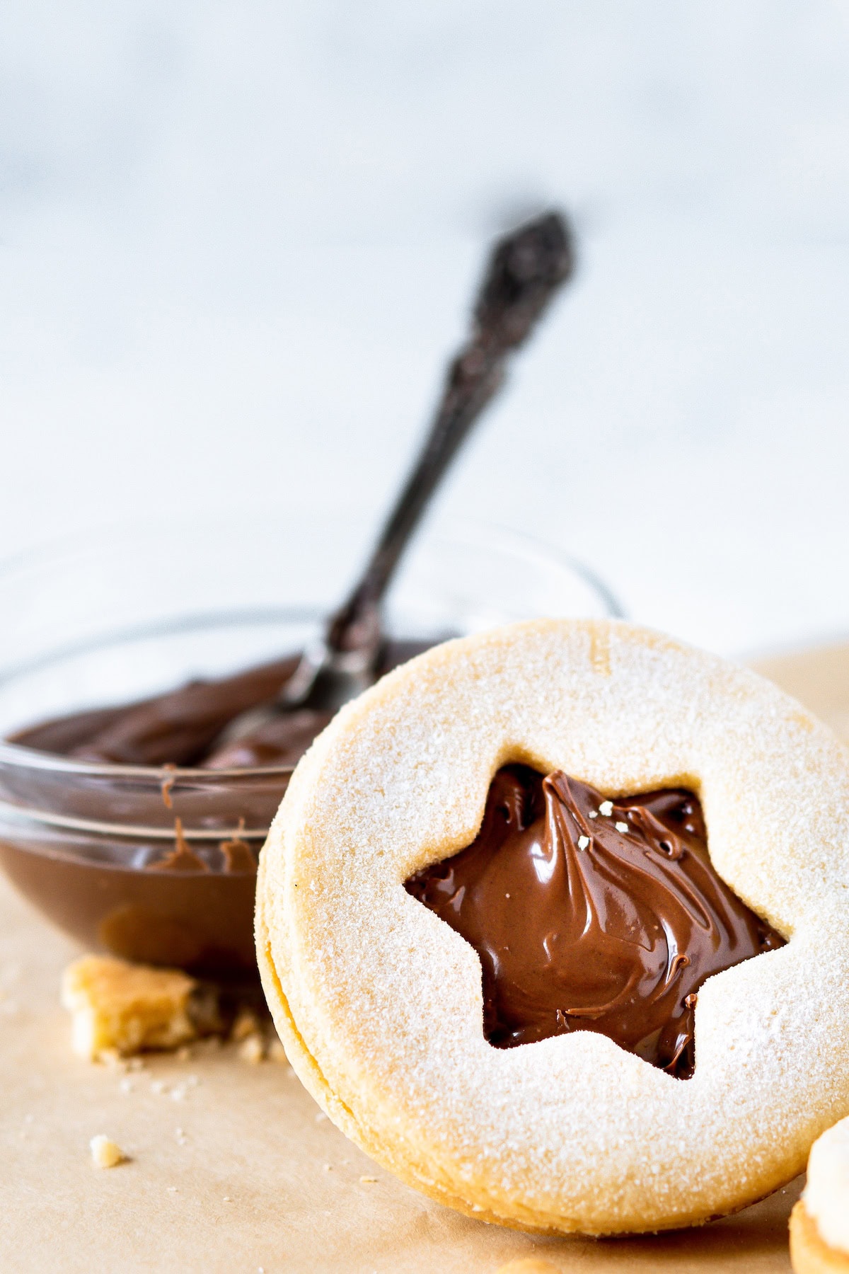 one Linzer cookie with a bowl of Nutella behind it