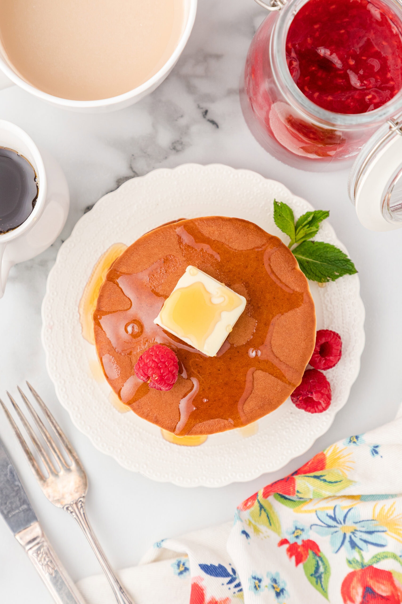 A stack of banana protein pancakes ready to be enjoyed. On a plate with a fork & knife next to the pancakes