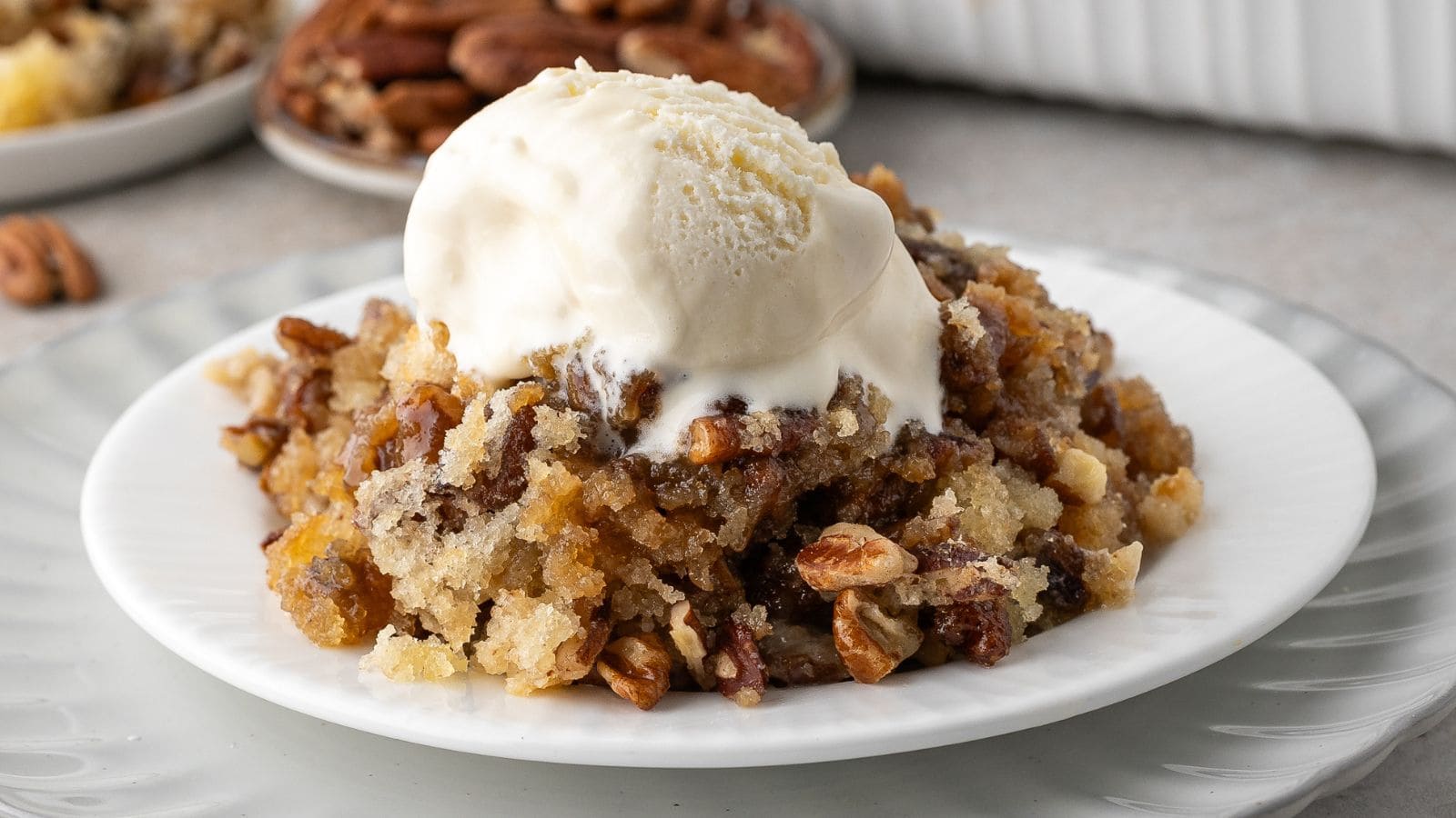 pecan pie cobbler topped with vanilla ice cream on a white plate