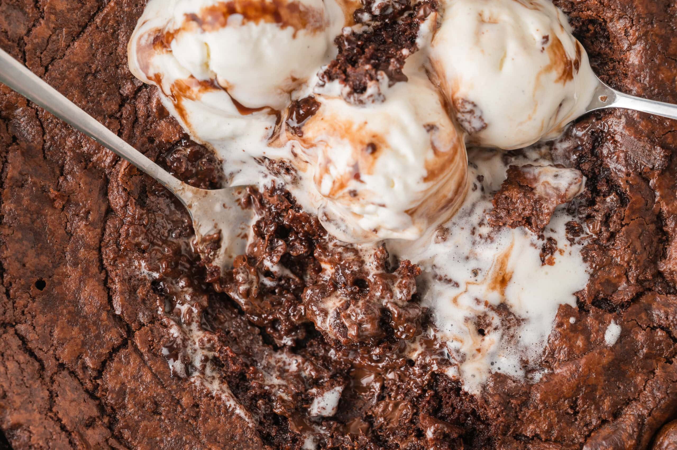Close up brownie skillet with gooey chocolate and melted vanilla ice cream with a spoon