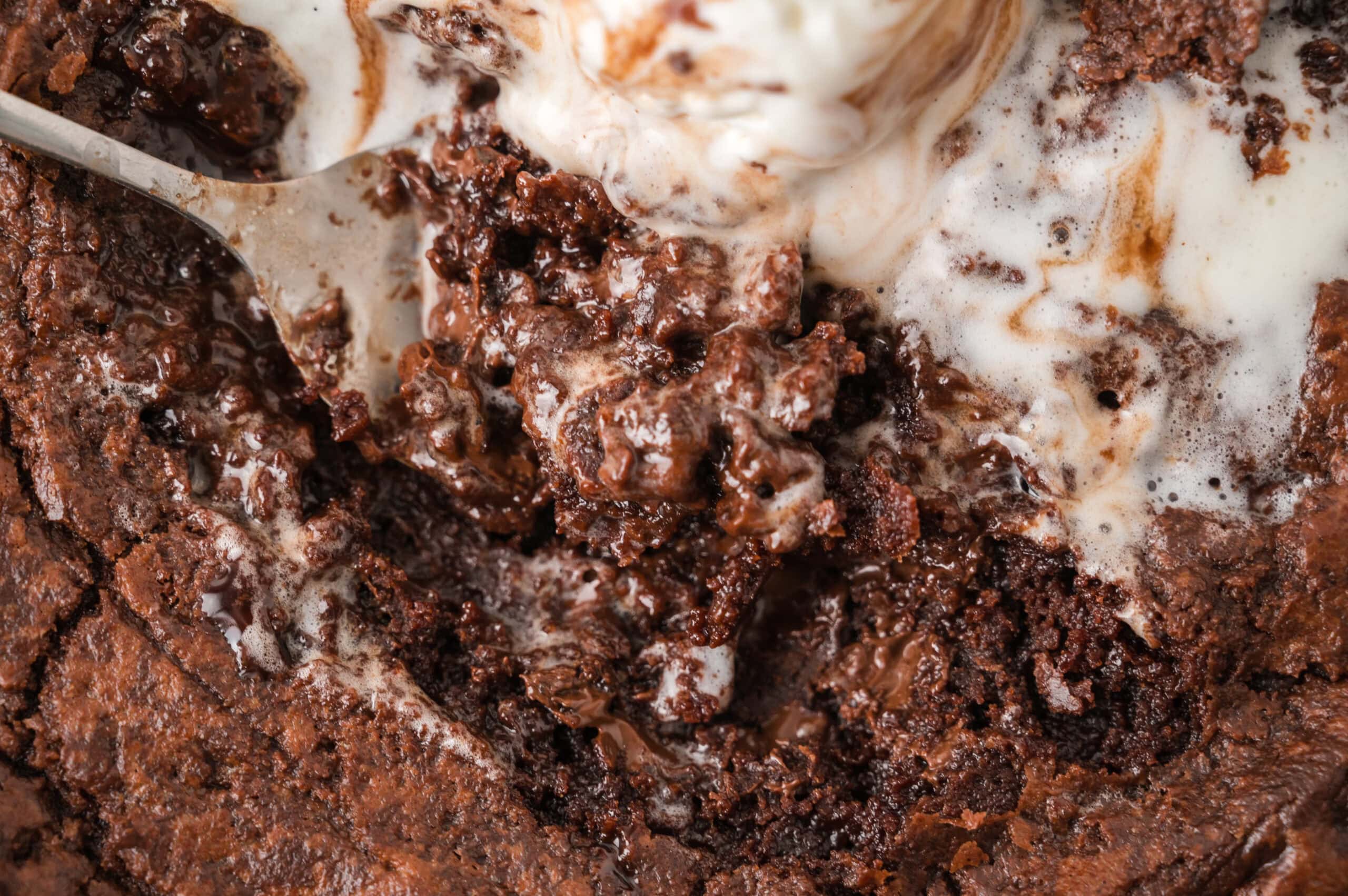 Close up of a spoonful of the baked skillet, with gooey chocolate and melted vanilla ice cream