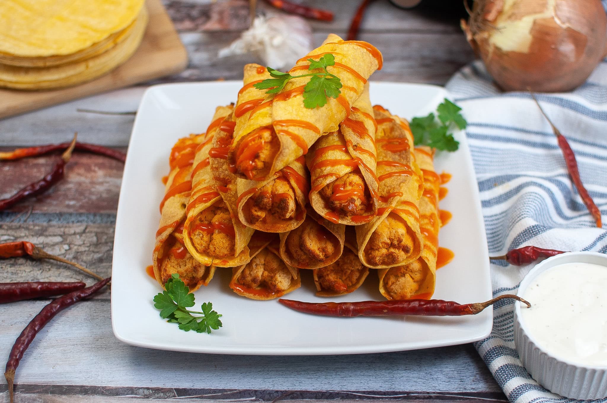 A plate with a stack of air fryer buffalo chicken taquitos, drizzled with hot sauce, ready to be dipped in ranch sauce and enjoyed