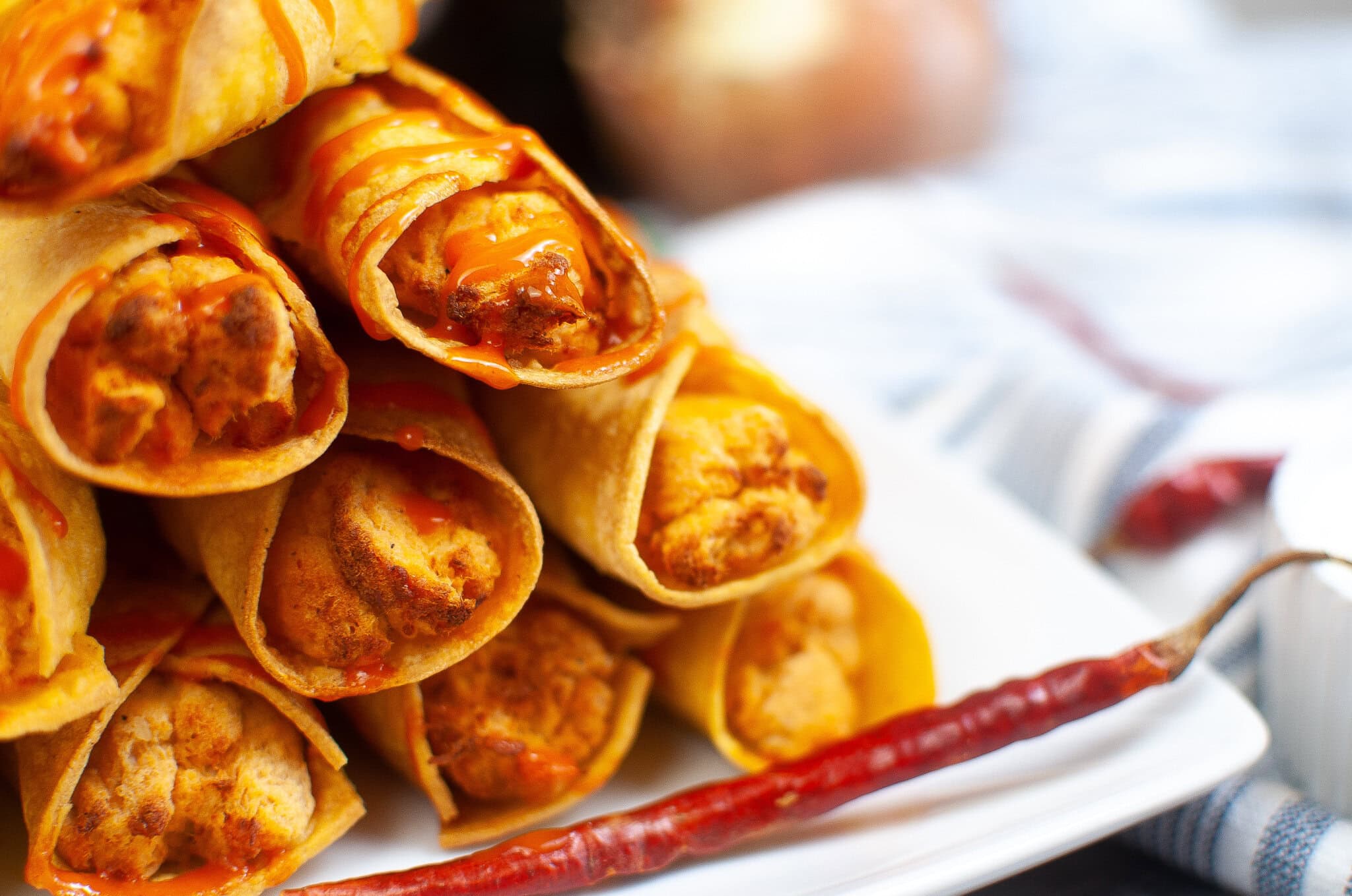 A stack of chicken taquitos, drizzled with hot sauce, ready to be enjoyed