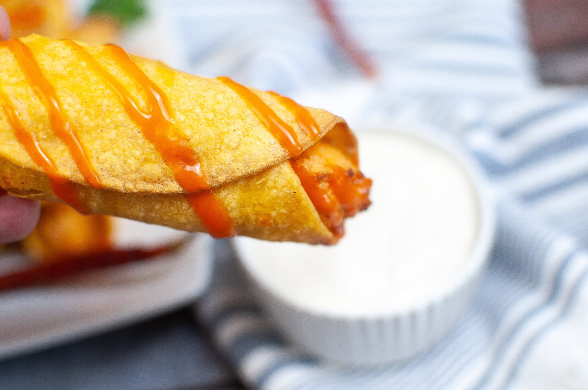 Close up of a chicken taquito from the air fryer and drizzled with hot sauce.