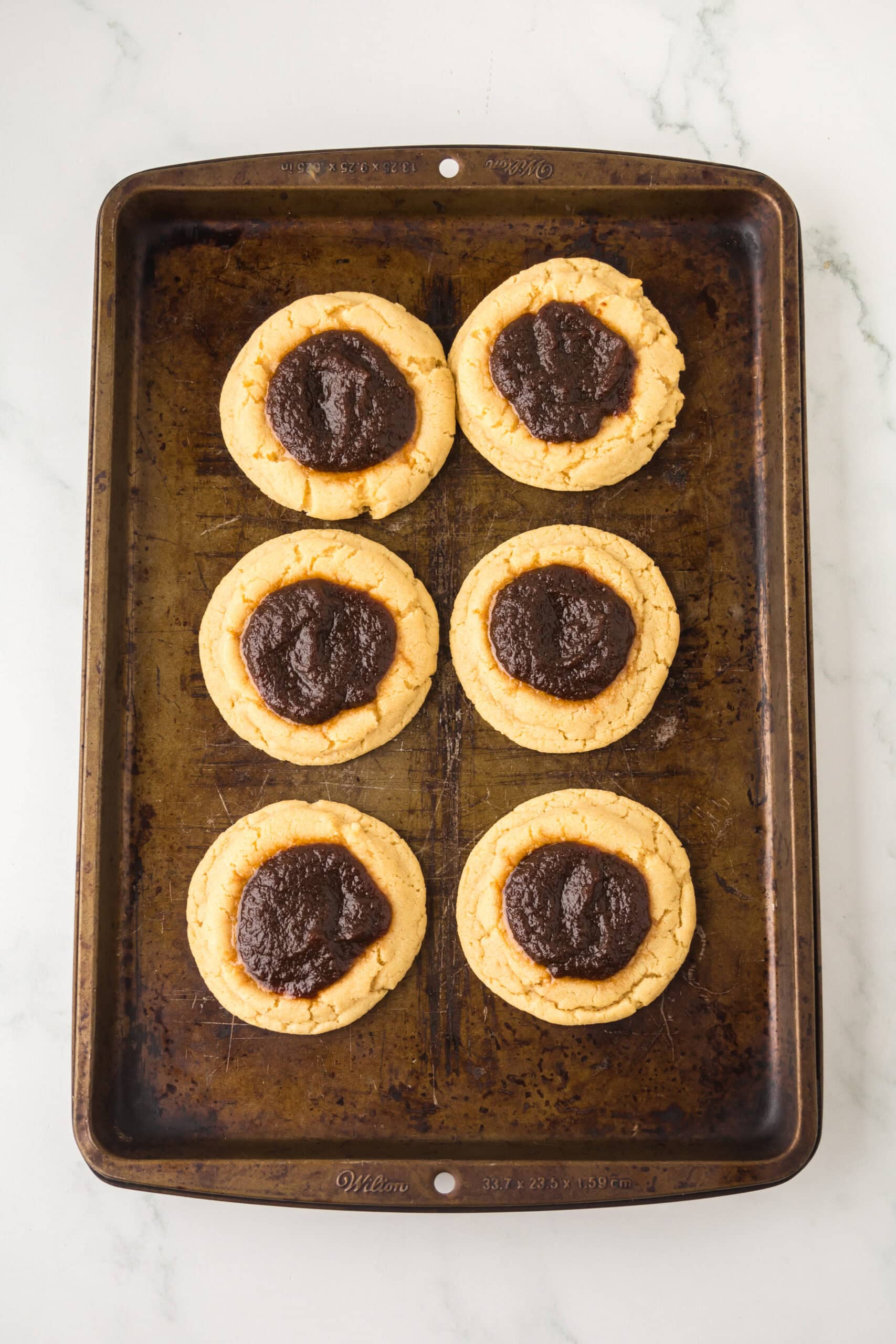 Baked apple butter thumbprint cookies on a baking sheet cooling