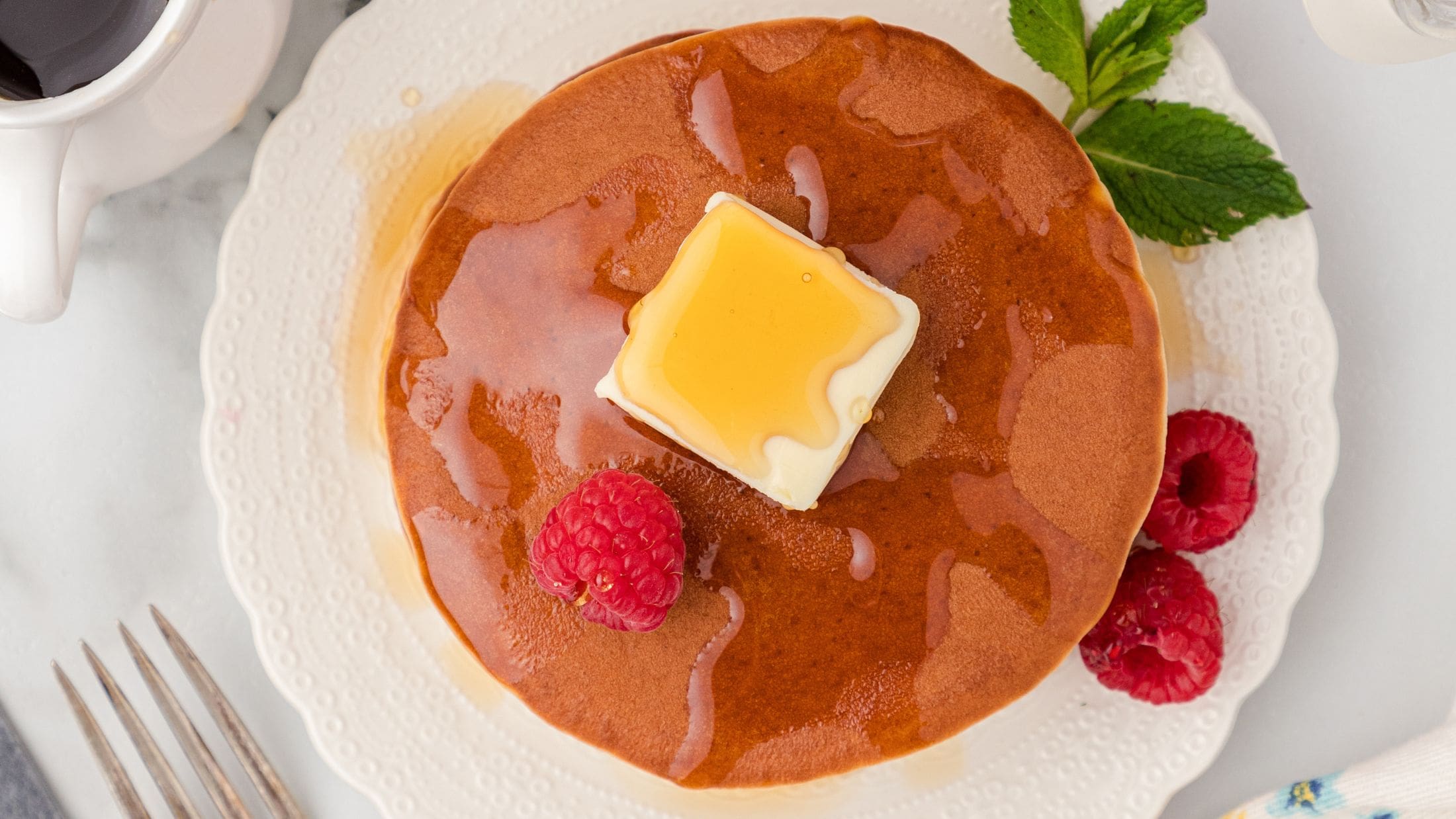 Banana protein pancakes on a plate, served, topped with butter, syrup and raspberries