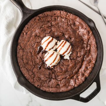 Brownie skillet all baked and ready to be enjoyed, 3 scoops of vanilla ice cream on top with drizzle of chocolate sauce