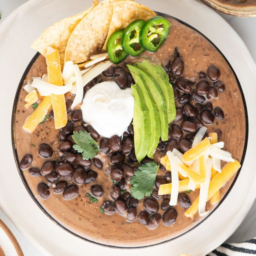 easy black bean soup with canned black beans, sliced avocados, shredded cheese, sour cream, sliced jalapenos, and tortilla chips in a large bowl
