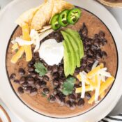 easy black bean soup with canned black beans, sliced avocados, shredded cheese, sour cream, sliced jalapenos, and tortilla chips in a large bowl