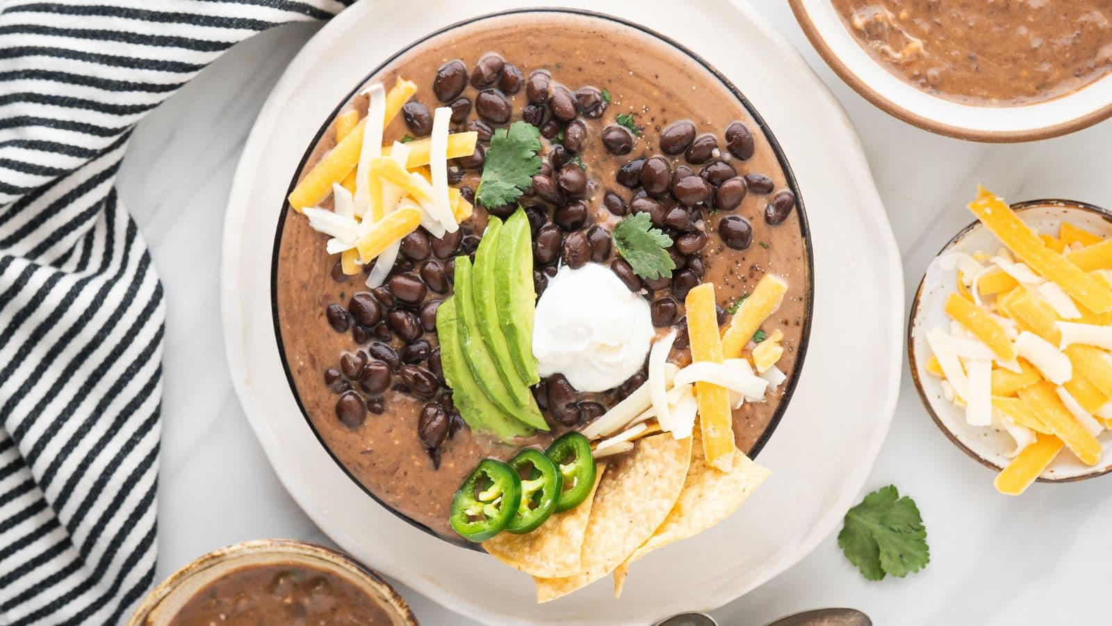 easy black bean soup with canned black beans, sliced avocados, shredded cheese, sour cream, sliced jalapenos, and tortilla chips in a white bowl