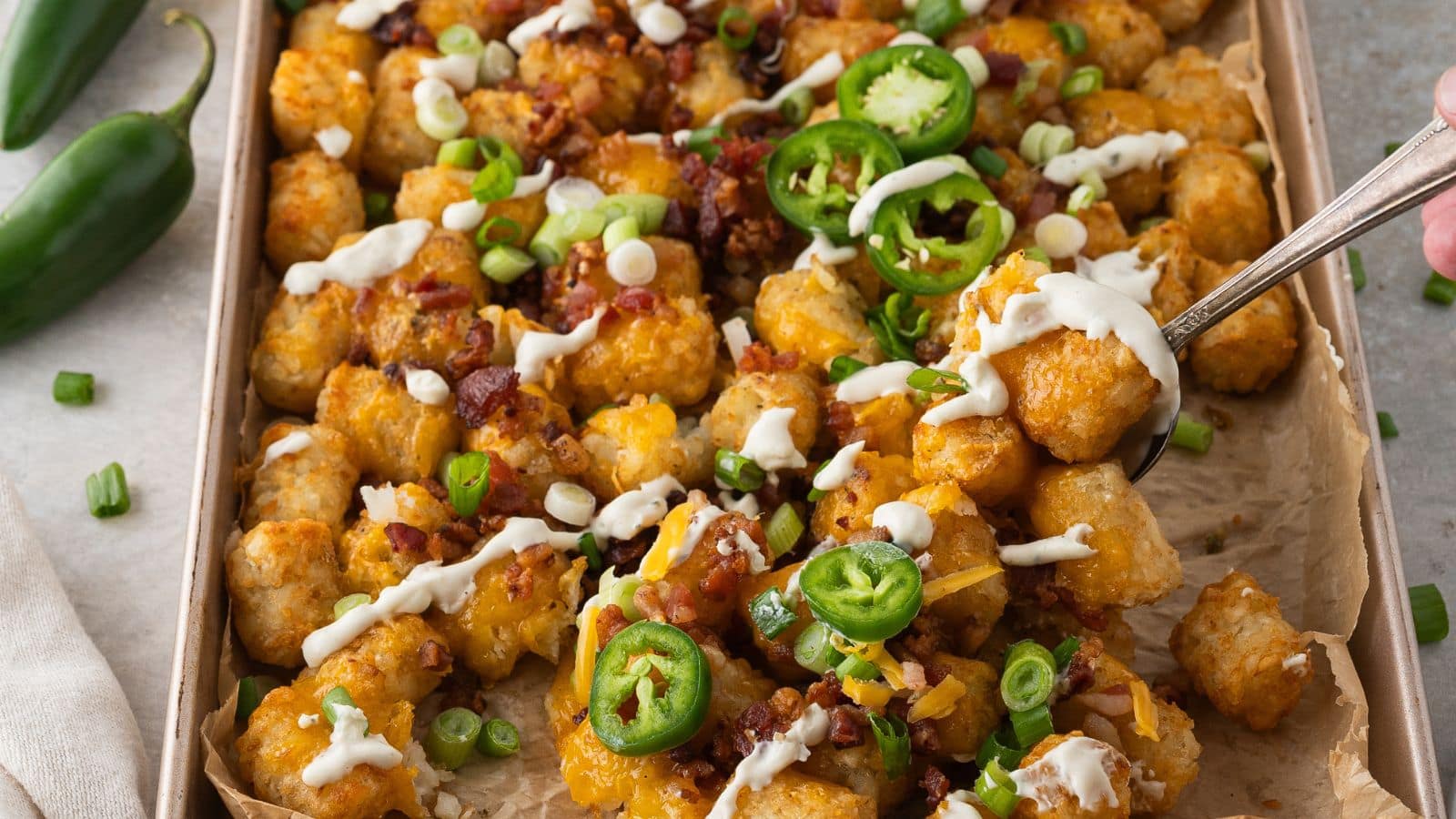 cheesy loaded tater tots with cheddar, bacon, and ranch sour cream with a spoon