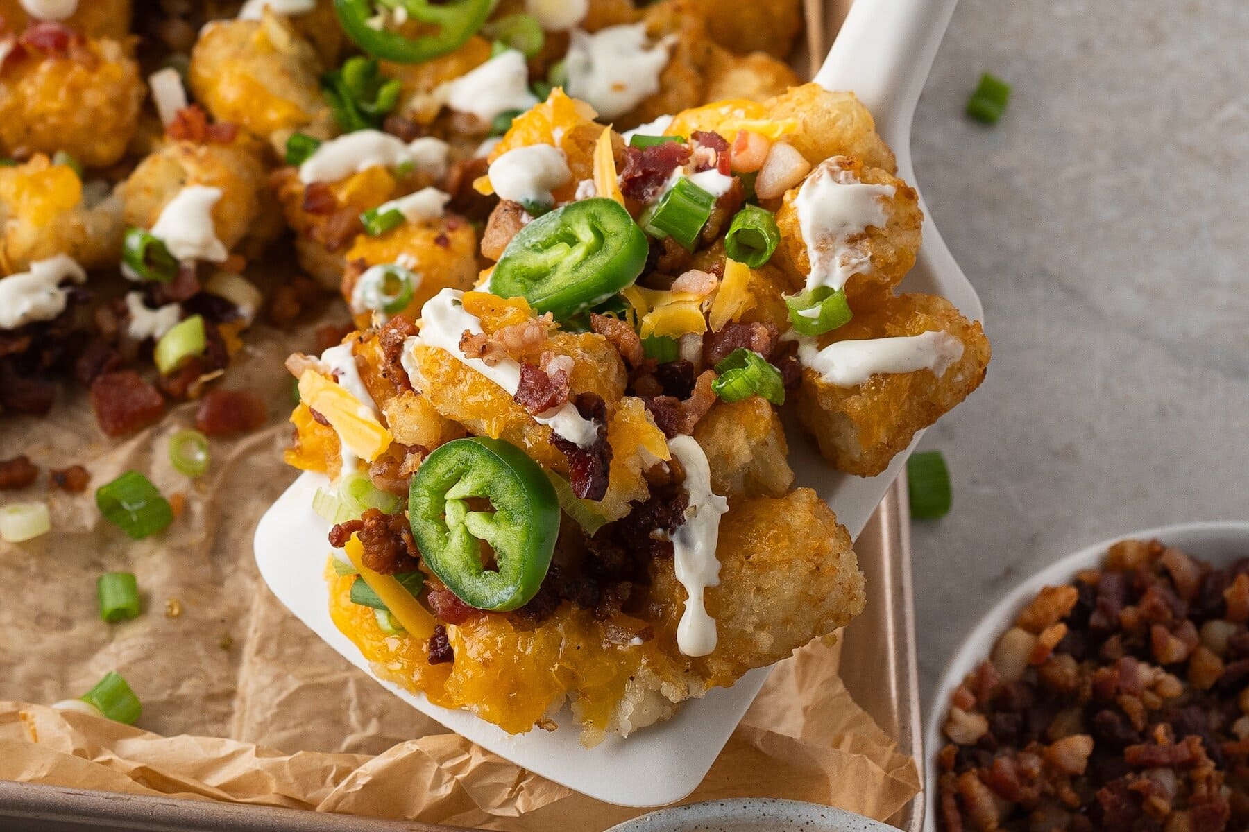 a close up of a spoonful of loaded tater tots with shredded cheddar and crumbled bacon