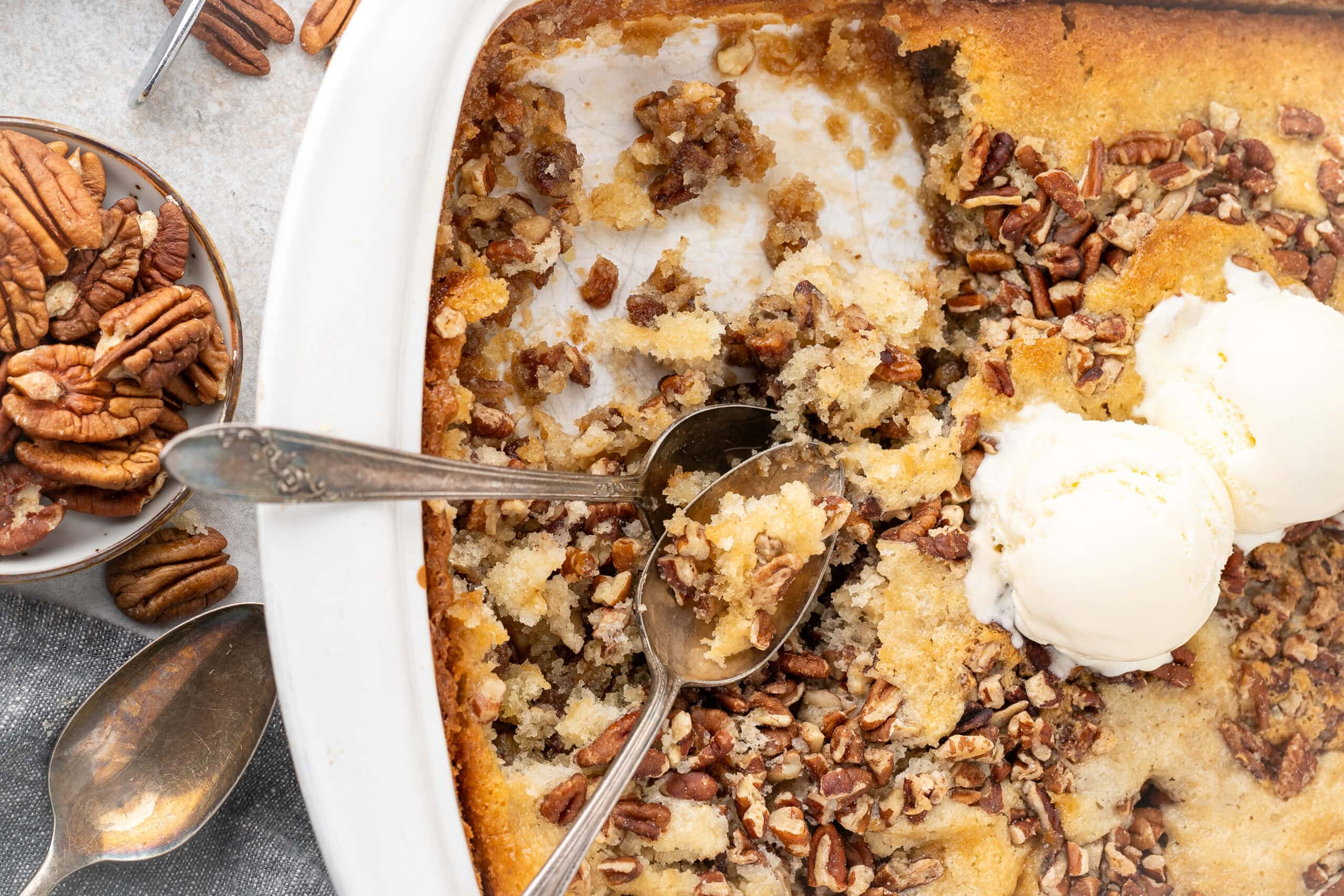 Two spoons laid in the pecan pie cobbler baking dish, ready to be enjoyed and shared