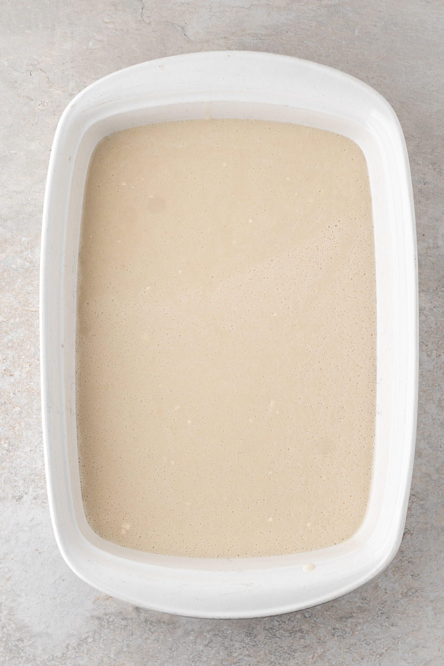 Flour, baking powder, salt and sugar has been whisked up with slowly adding milk and poured on top of melted butter in baking dish