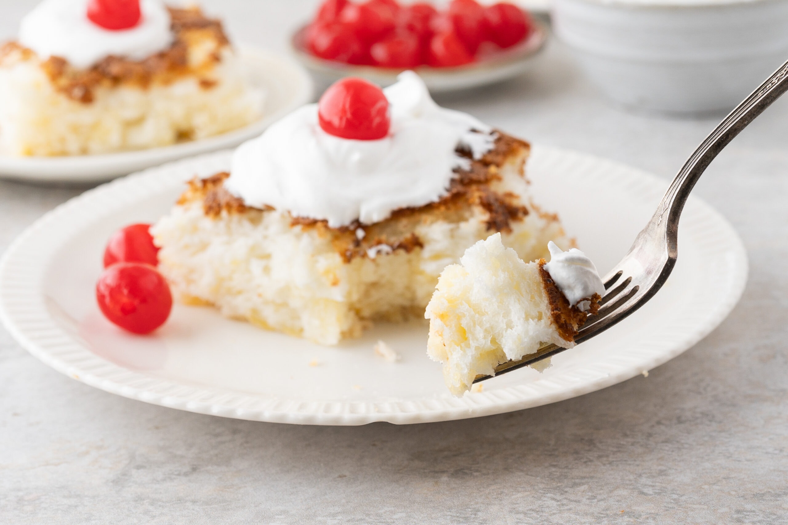 A slice of angel food cake, plated and a fork cutting a piece to enjoy